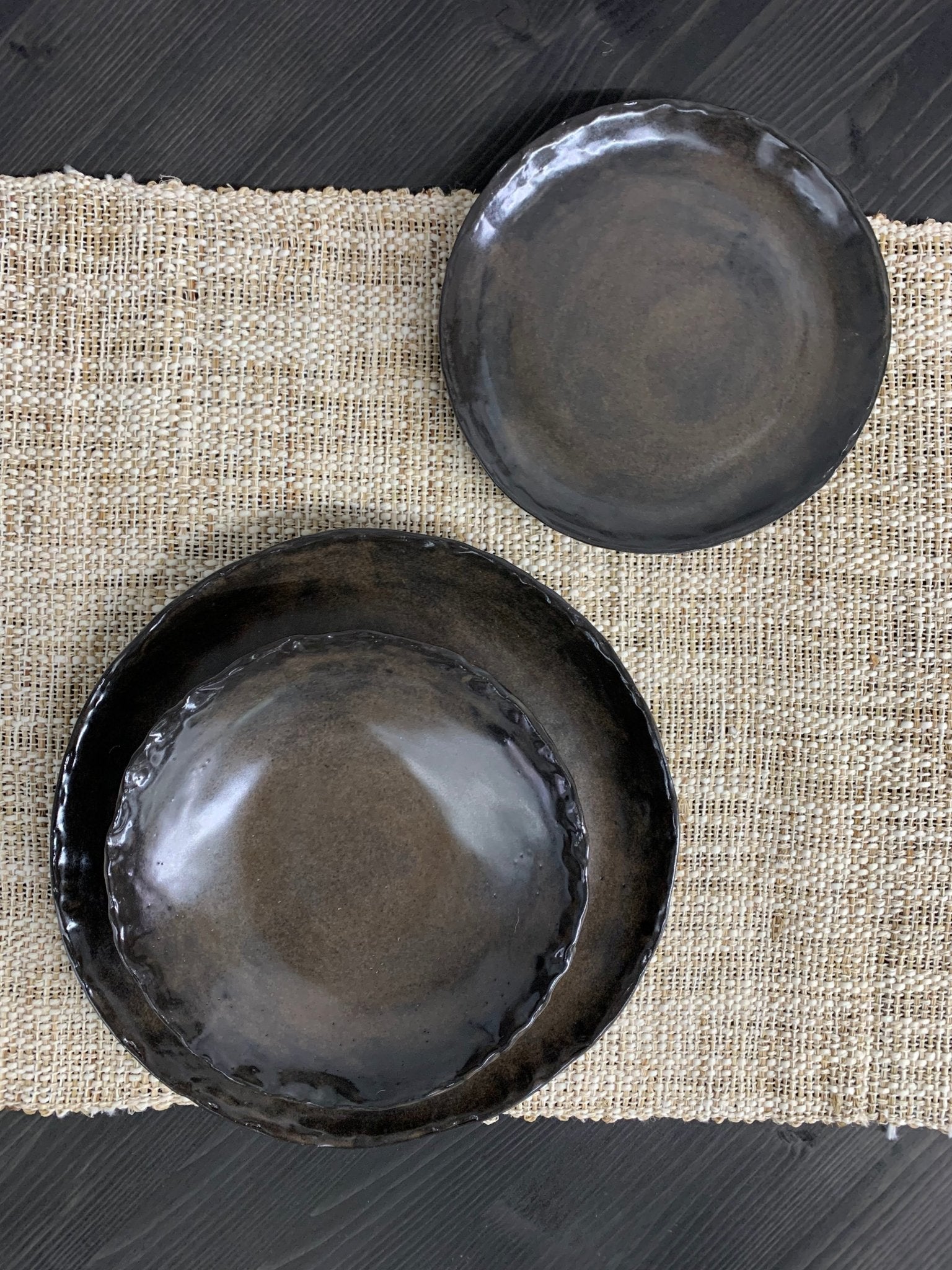 Black handmade ceramic dinnerware on a textured fabric surface