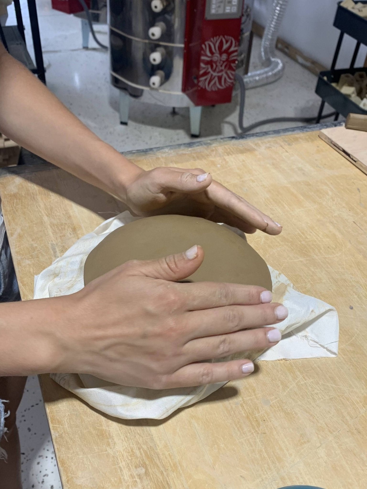 Person rolling out clay on a wooden surface with a pottery studio background