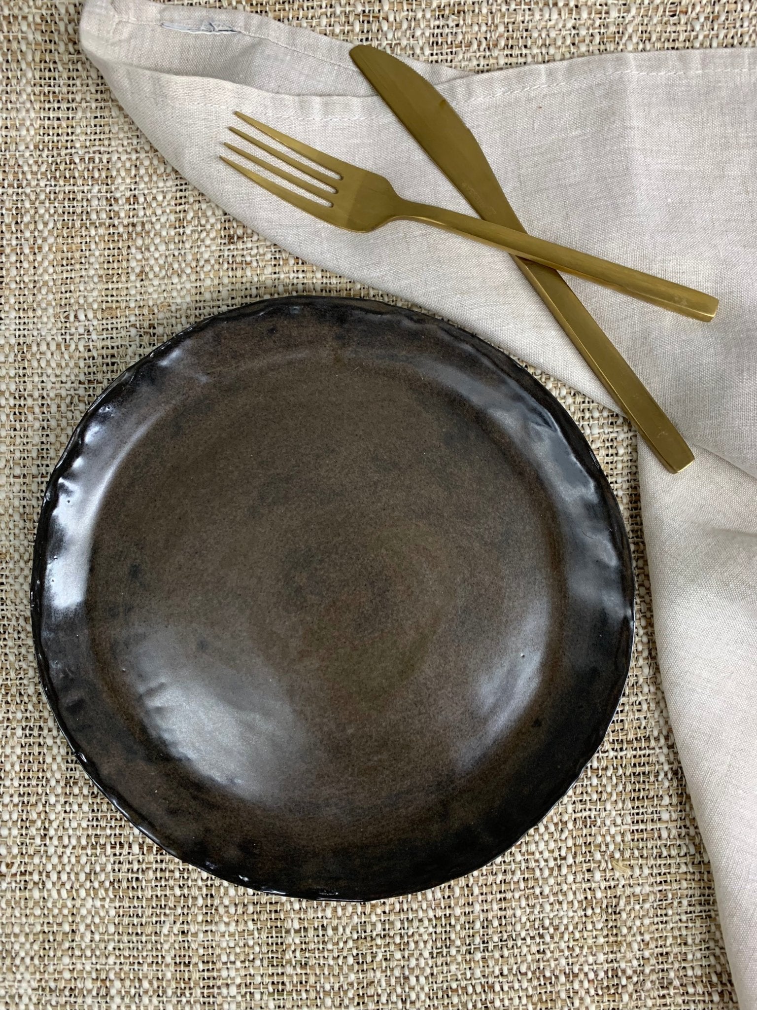 Brown ceramic plate with gold fork and knife on a textured surface