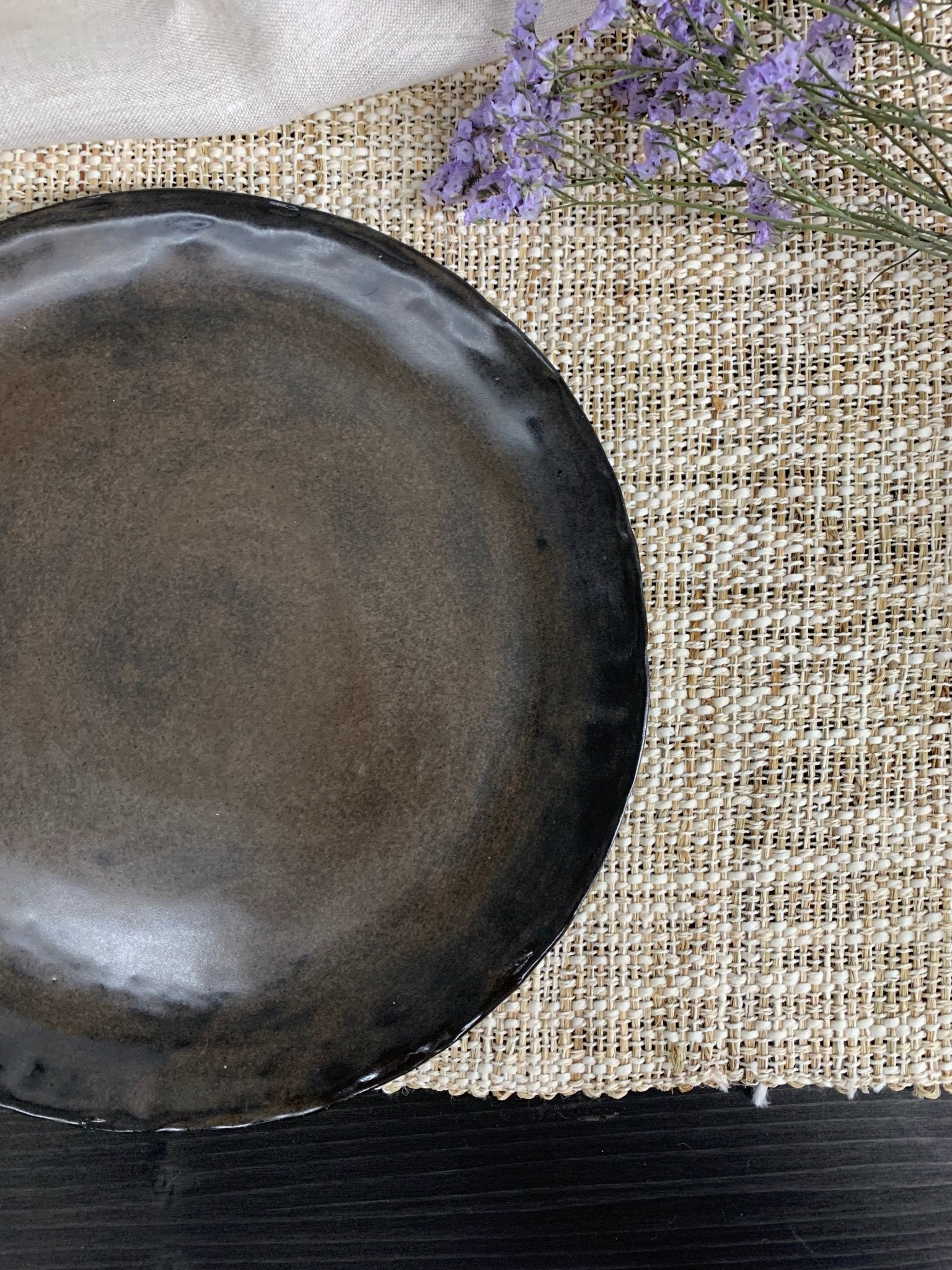 Dark brown ceramic plate on a textured surface with lavender flowers