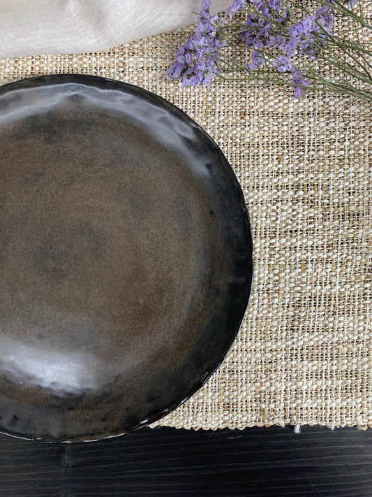 Dark brown ceramic plate on a textured surface with lavender flowers