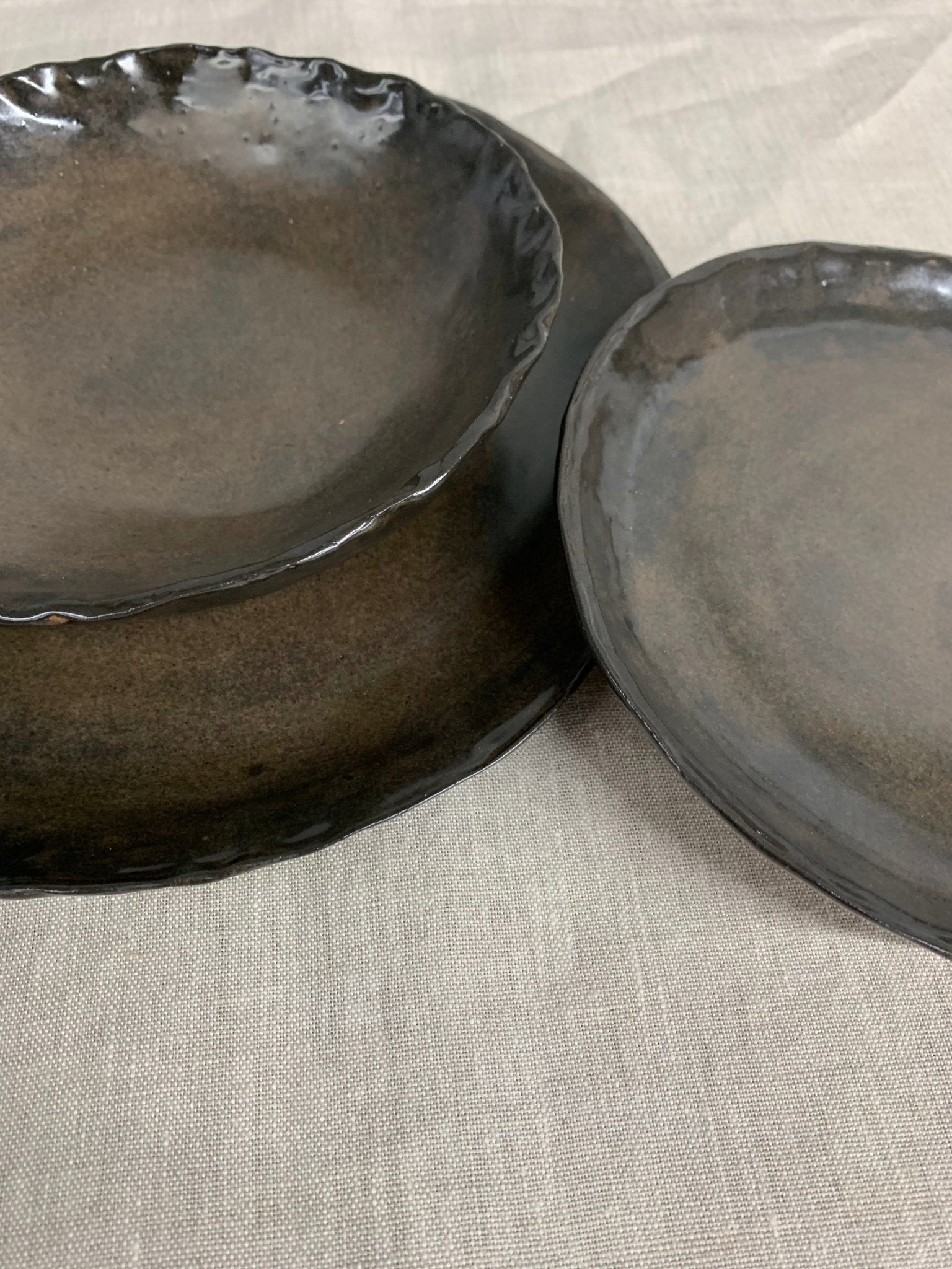Two handmade brown ceramic plates on a textured beige surface