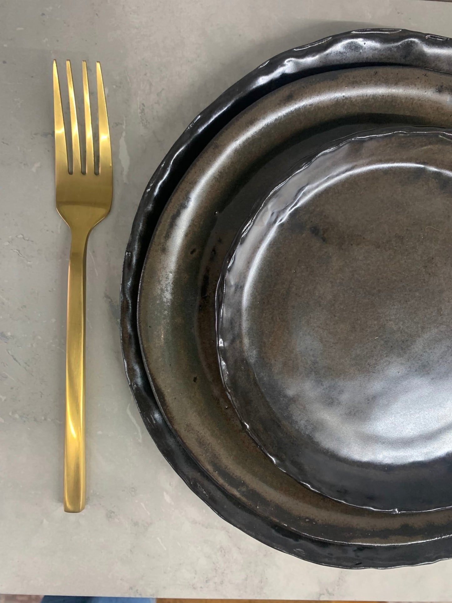Gold fork next to a place setting of 3 brown handcrafted plates on a marble surface
