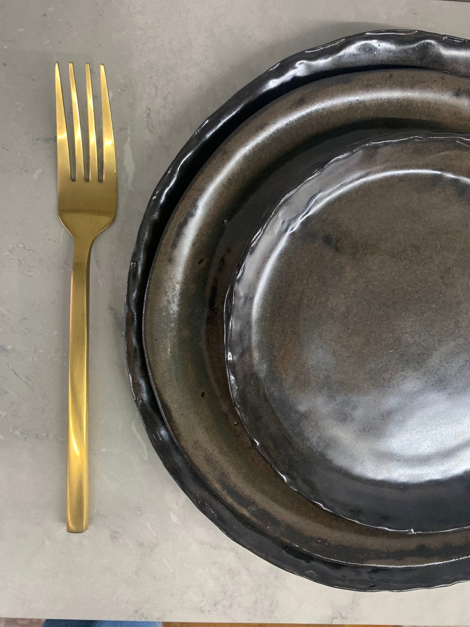 Gold fork next to a place setting of 3 brown handcrafted plates on a marble surface