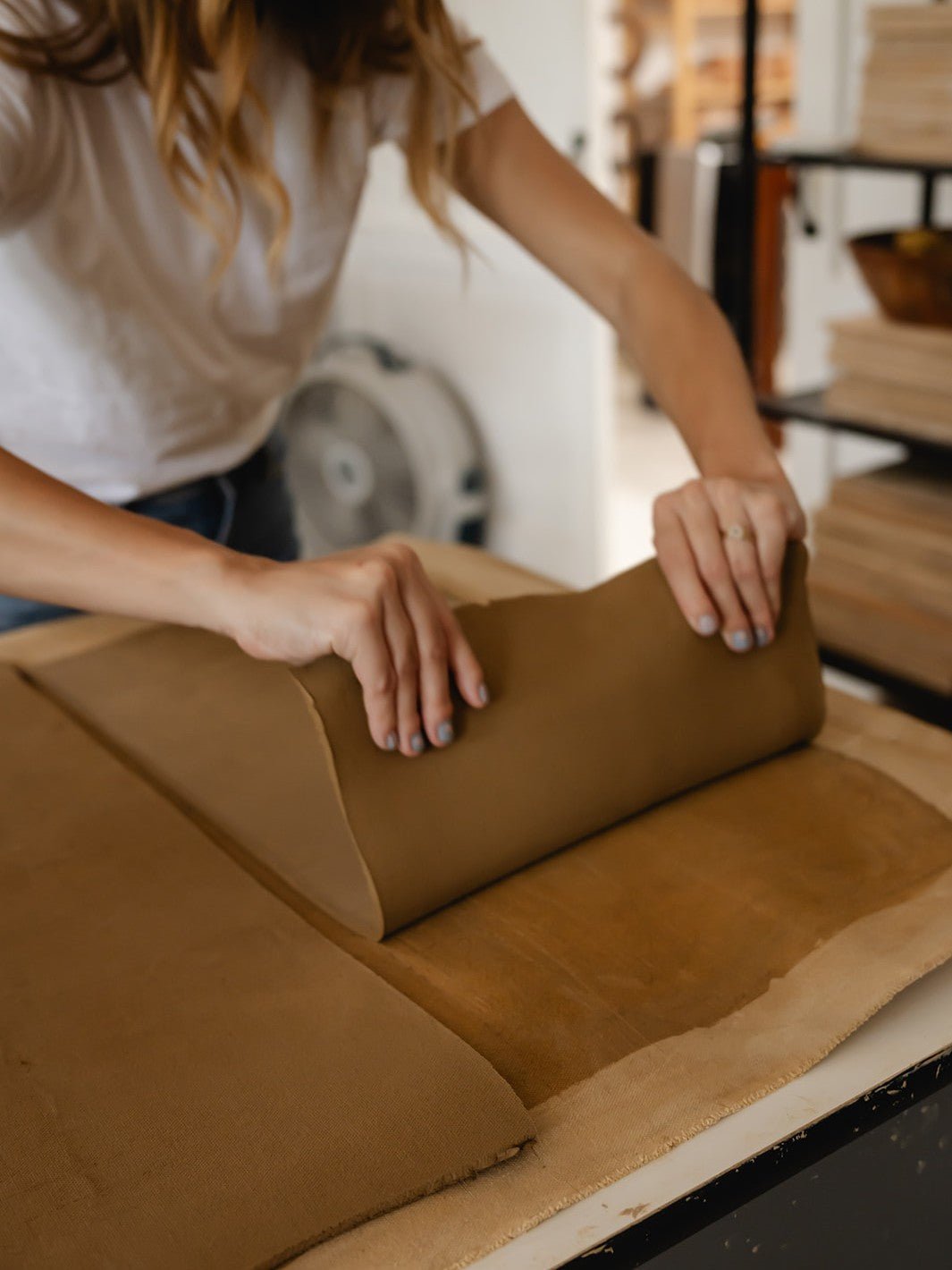 Person rolling out brown clay on a table in a art pottery studio