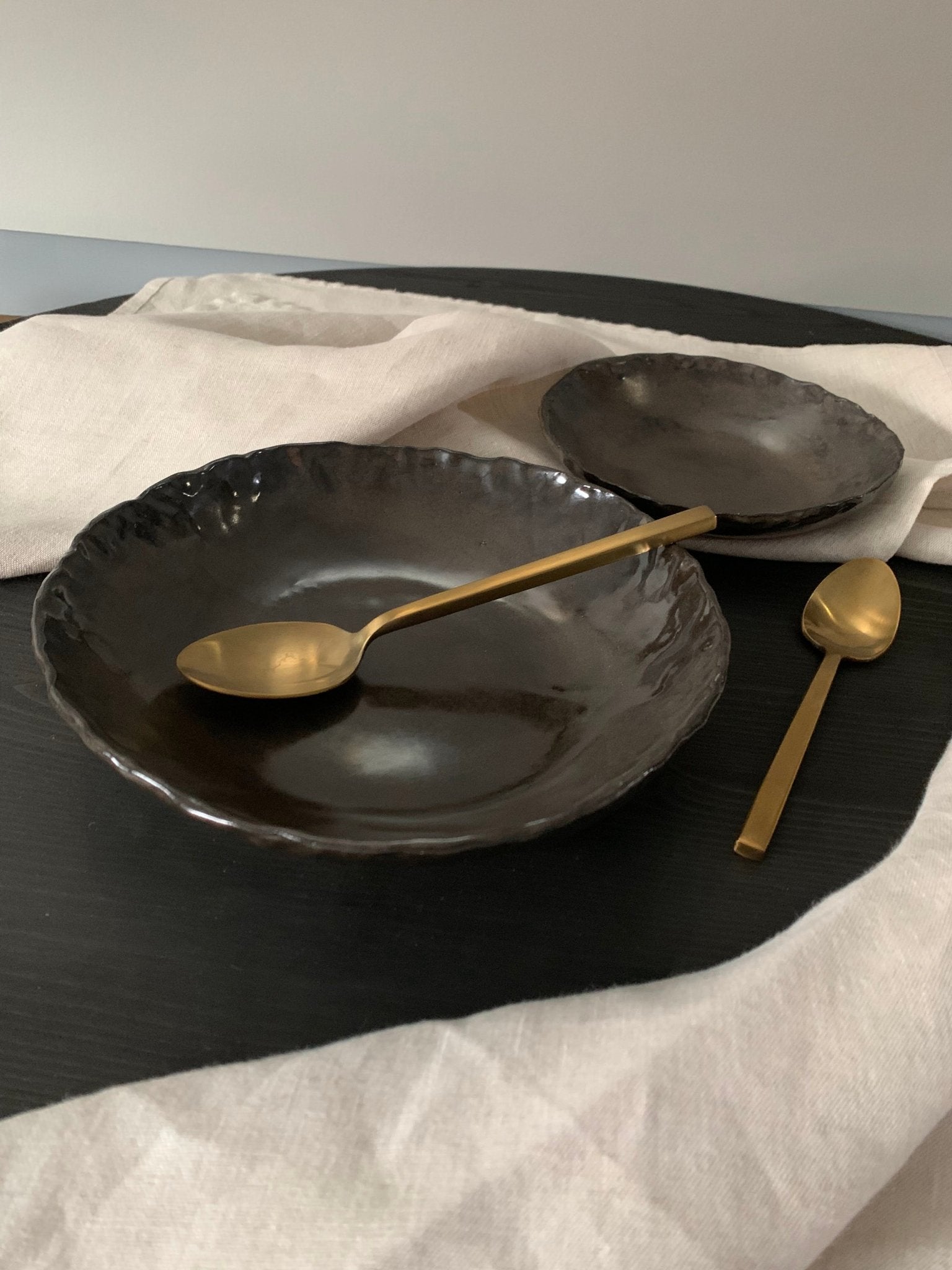 Black ceramic plates with gold spoons on a white cloth