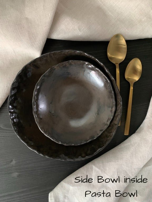 Set of black handmade ceramic bowls with gold spoons on a dark surface