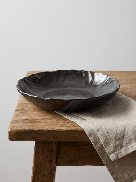 Black ceramic bowl on a wooden stool with a linen cloth