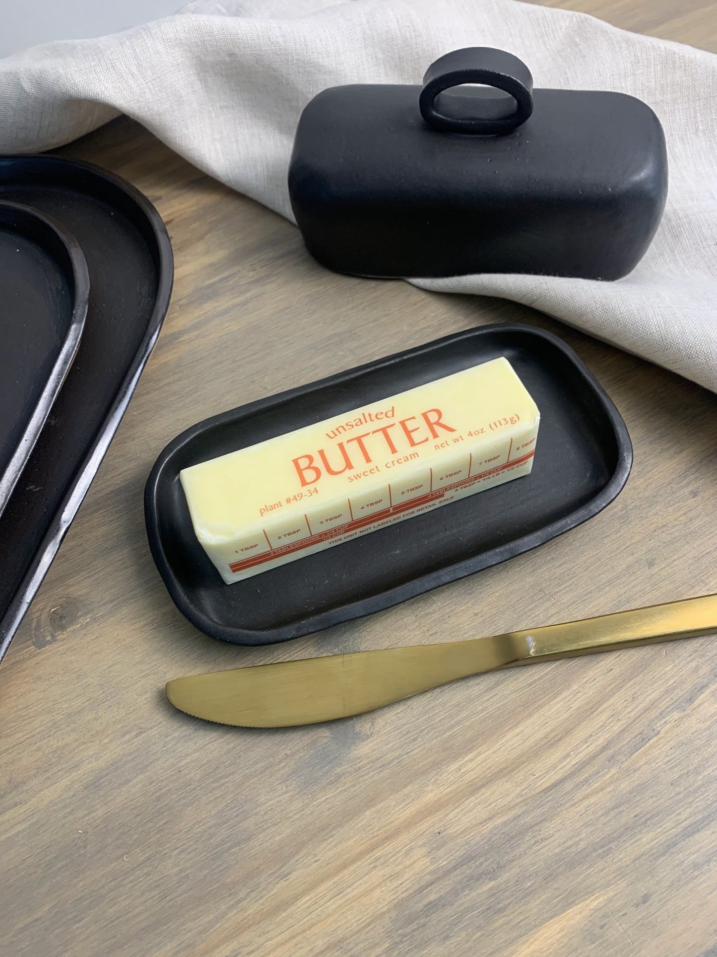 Handmade ceramic butter dish with a stick of butter and a knife on a wooden surface