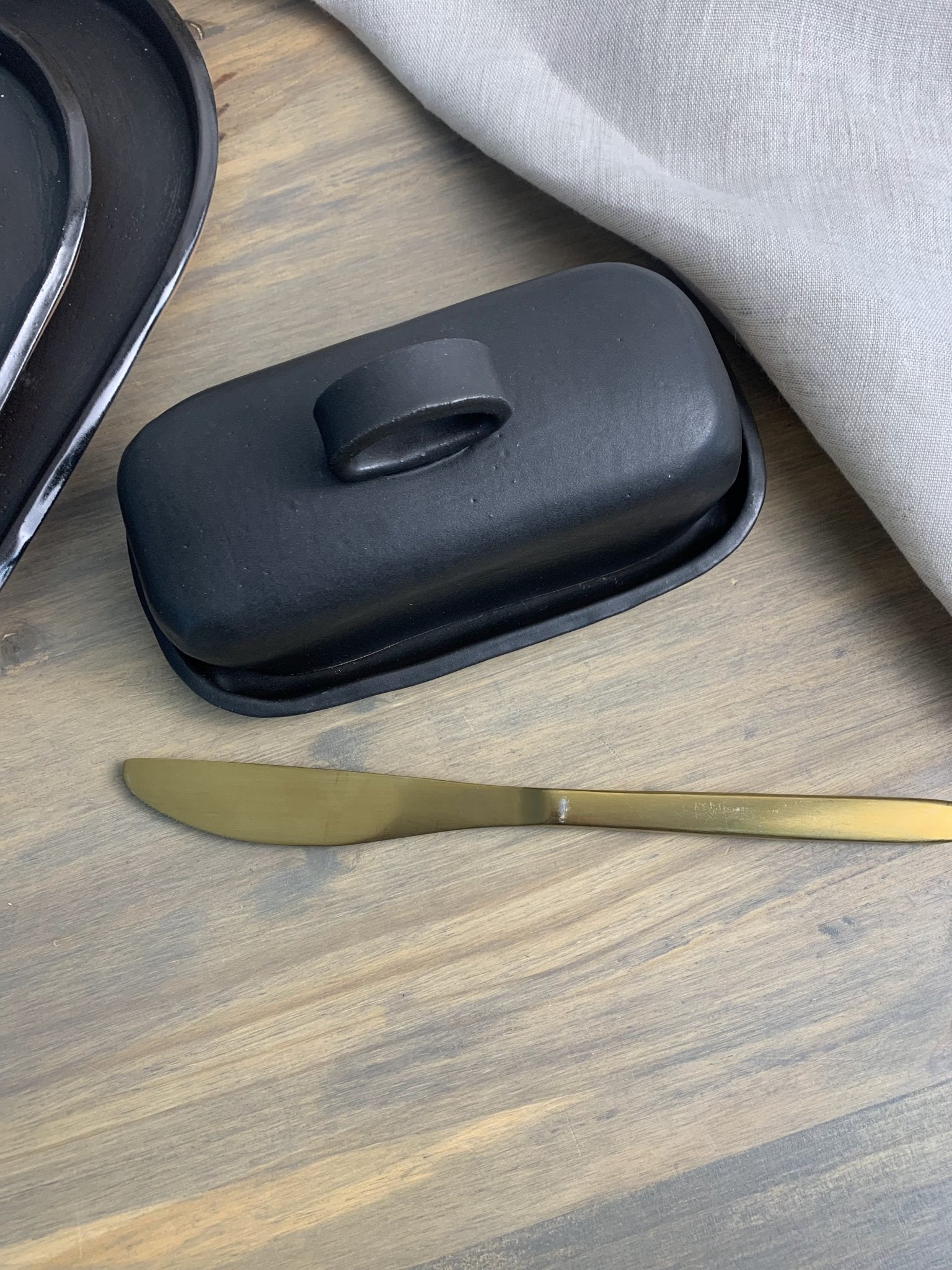 Handmade ceramic black butter dish with a gold knife on a wooden surface