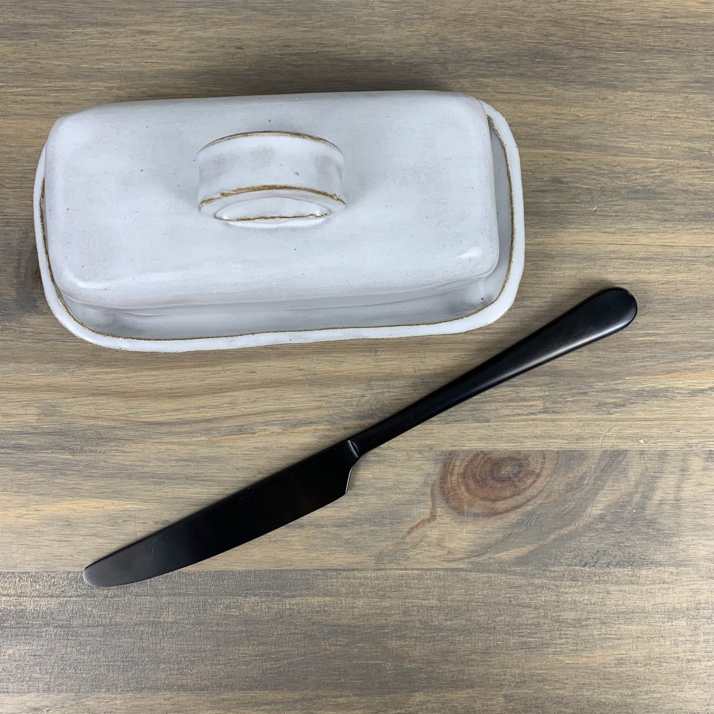 White ceramic butter dish with a black knife on a wooden surface