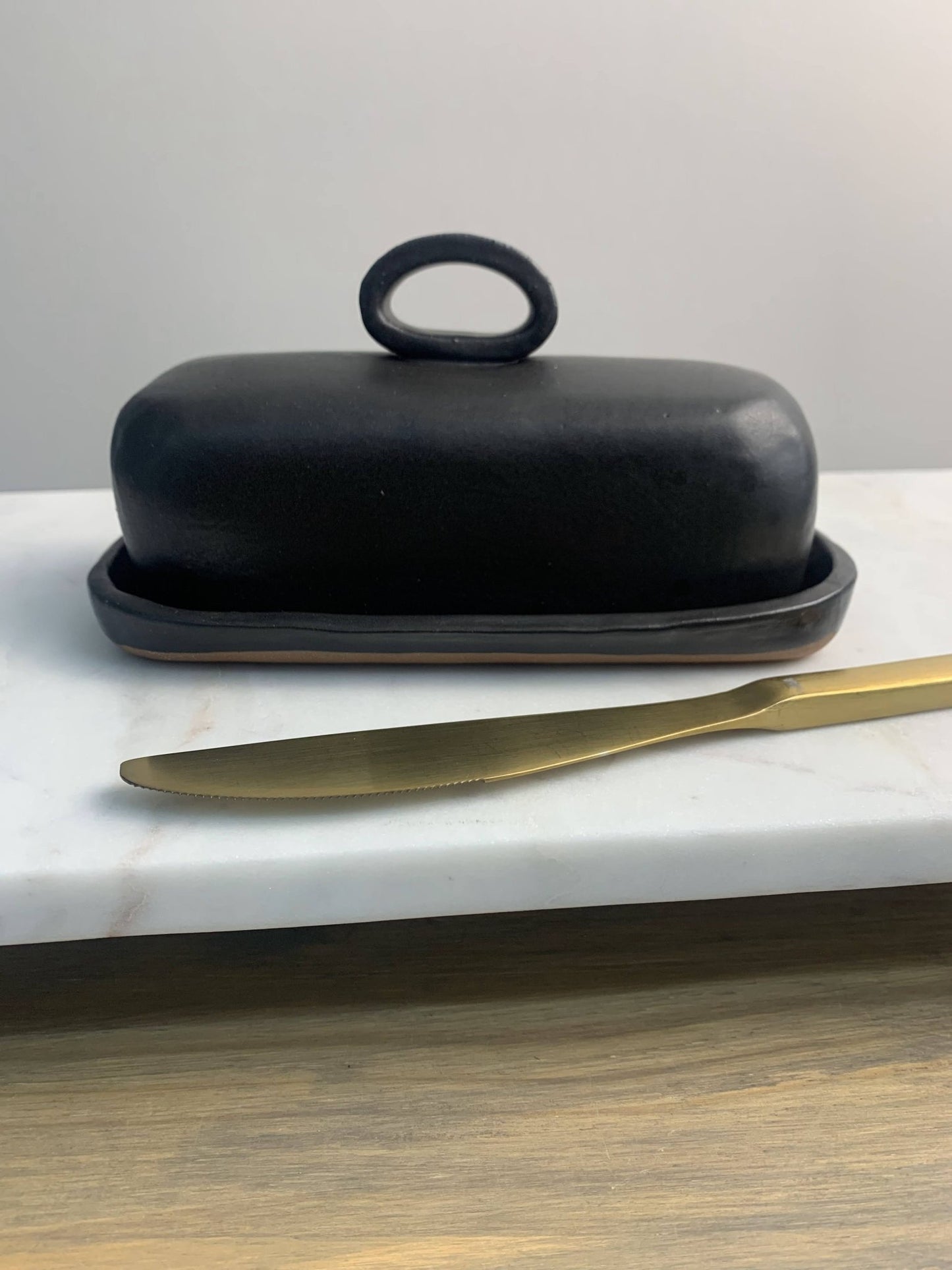 Handmade ceramic black butter dish with a gold knife on a marble surface