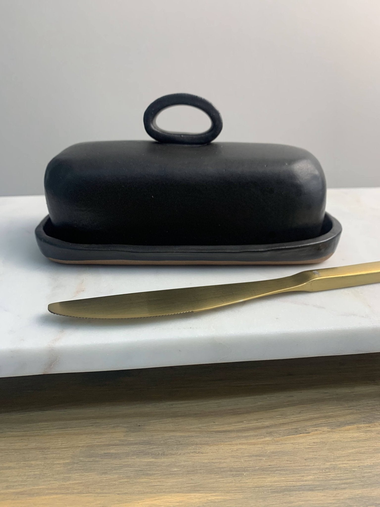 Handmade ceramic black butter dish with a gold knife on a marble surface