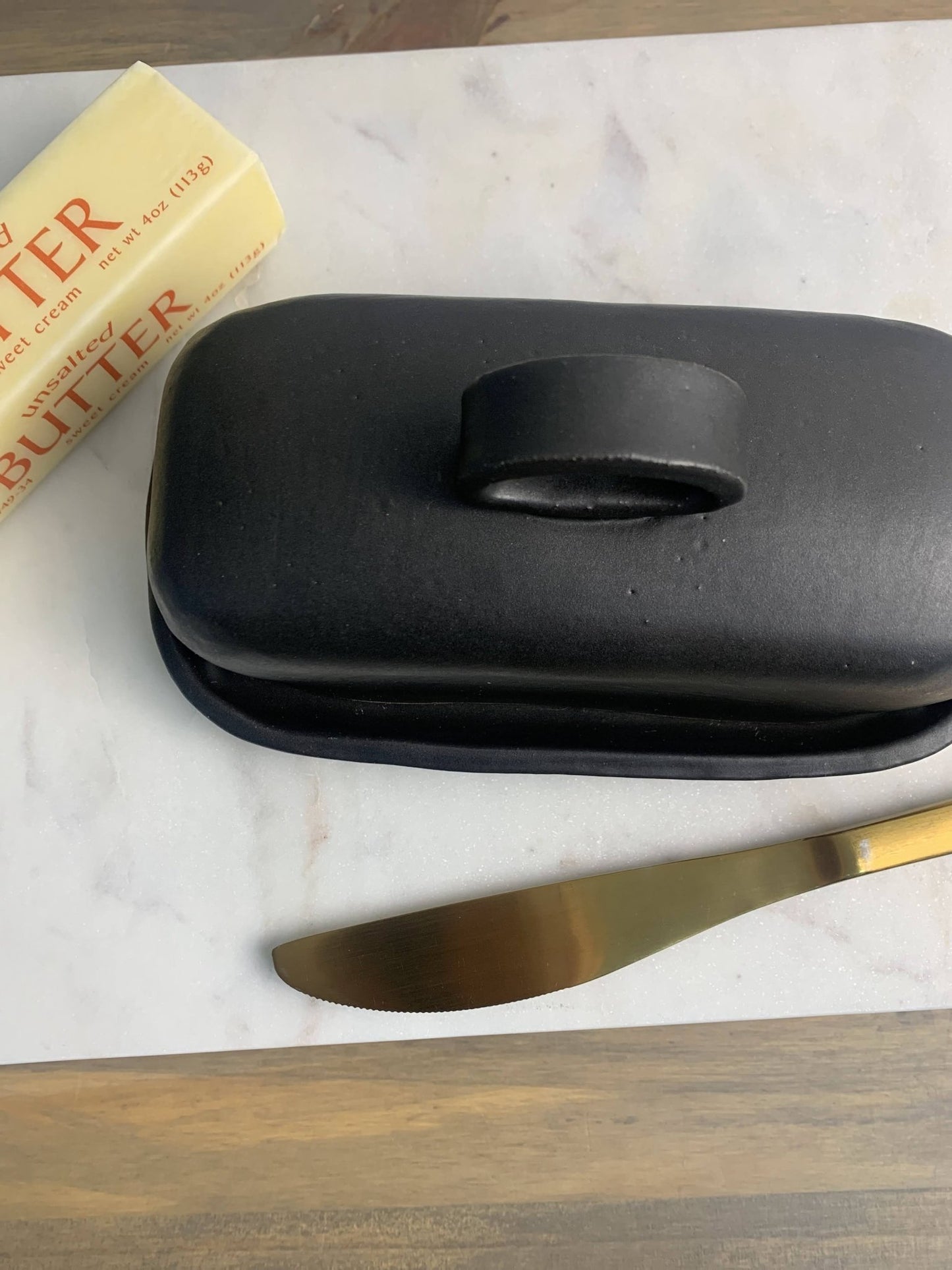 Handmade ceramic black dish on a marble surface with a bar of butter in the background
