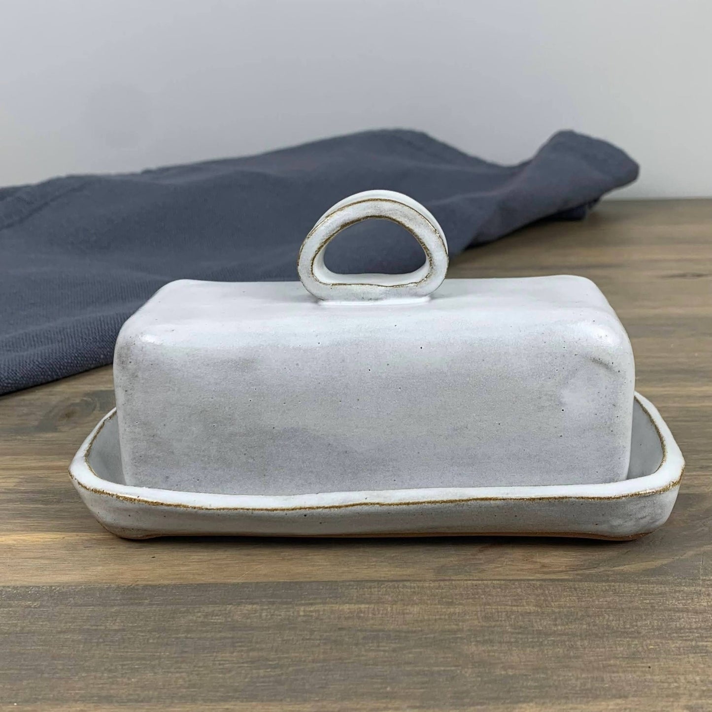 White handmade ceramic butter dish with lid on a wooden surface