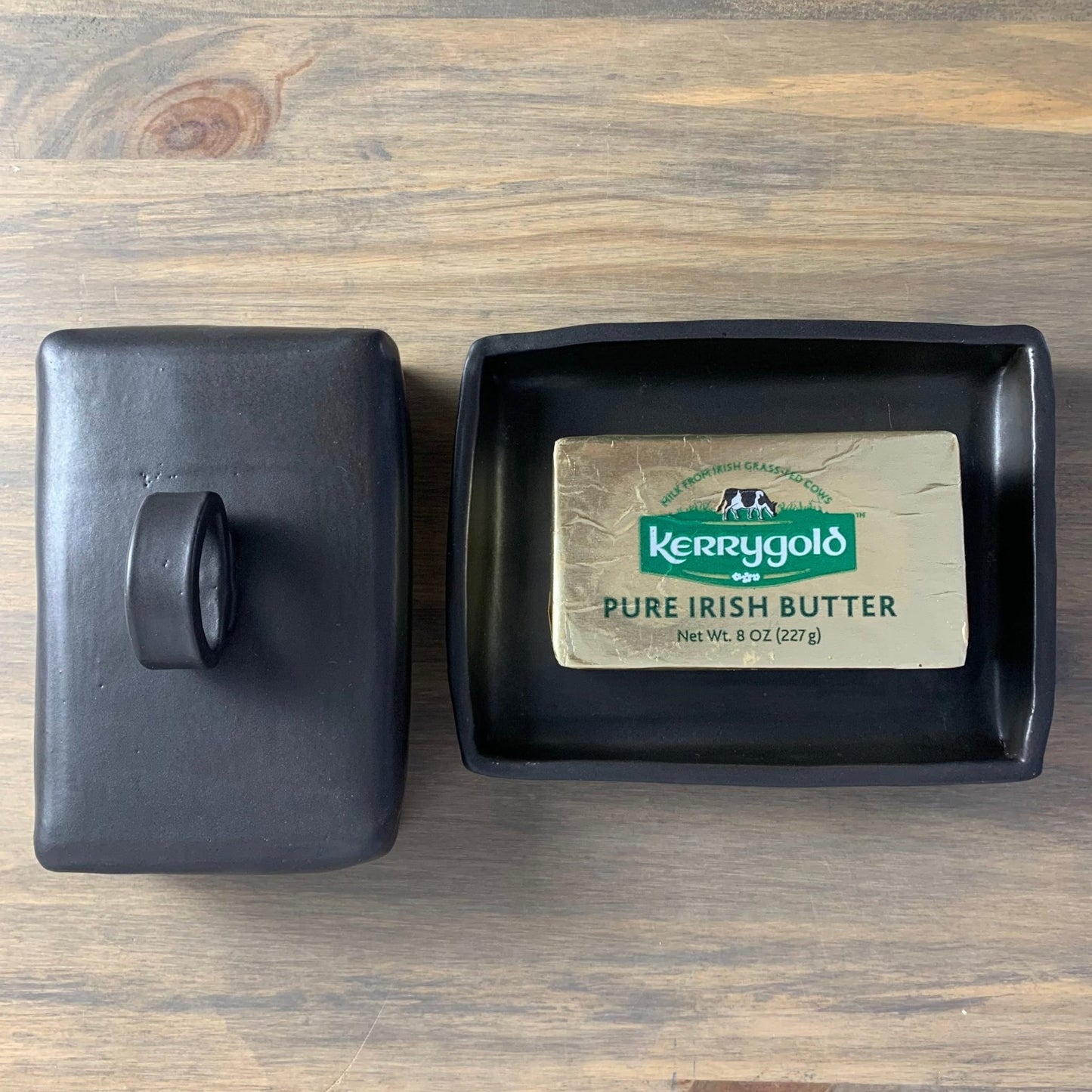 Kerrygold pure Irish butter bar in a black handmade ceramic butter dish on a wooden surface