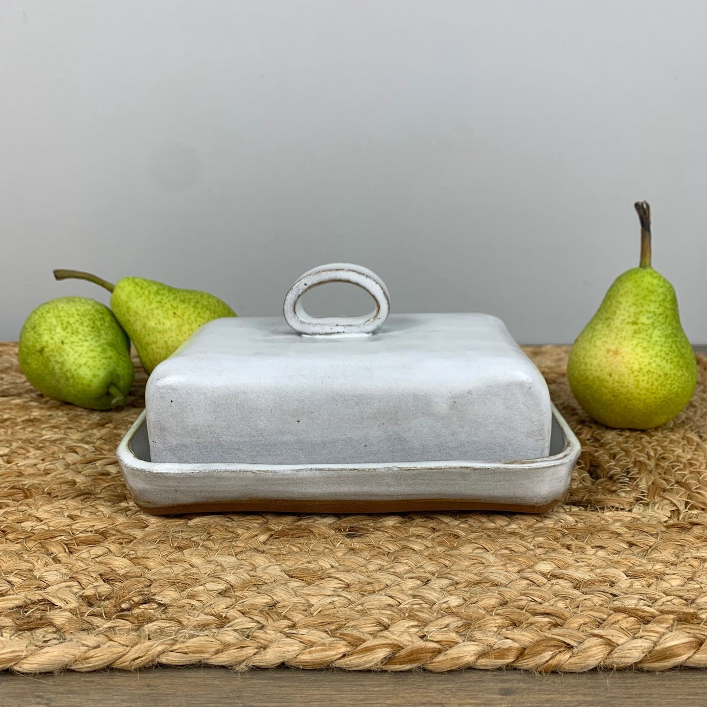 Handmade ceramic butter dish with a lid on a woven mat with pears