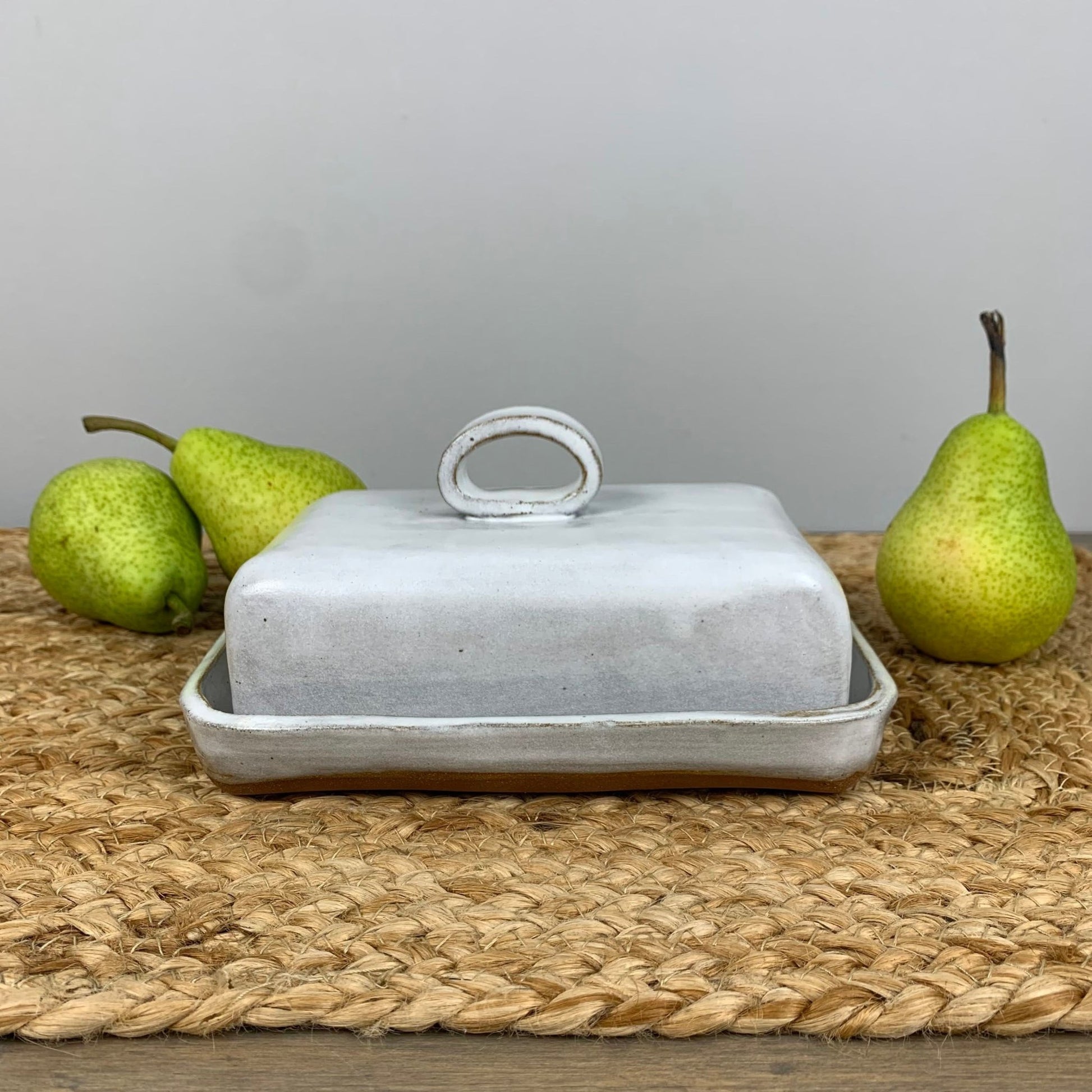 Handmade ceramic butter dish with a lid on a woven mat with pears