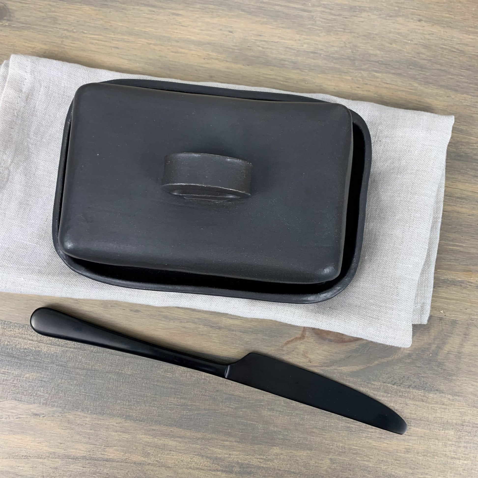 Black handmade ceramic butter dish with lid and knife on a wooden surface