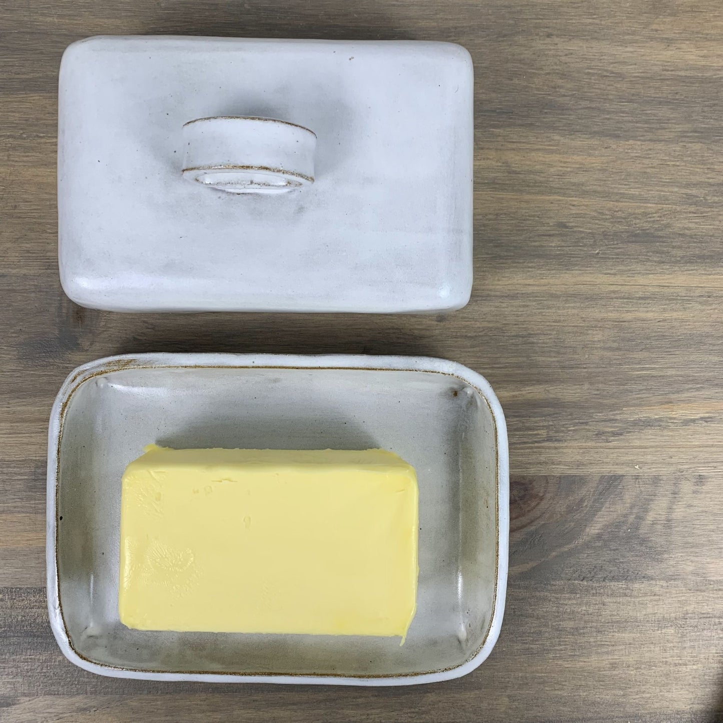 Handmade ceramic butter dish with a stick of butter inside on a wooden surface