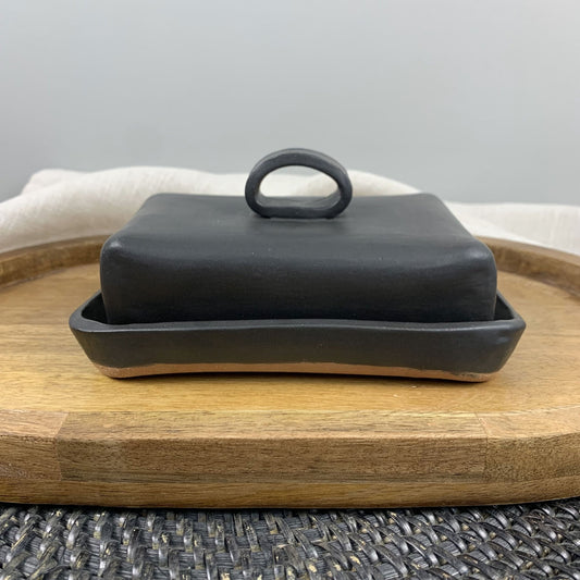 Black handmade ceramic butter dish with lid on a wooden board