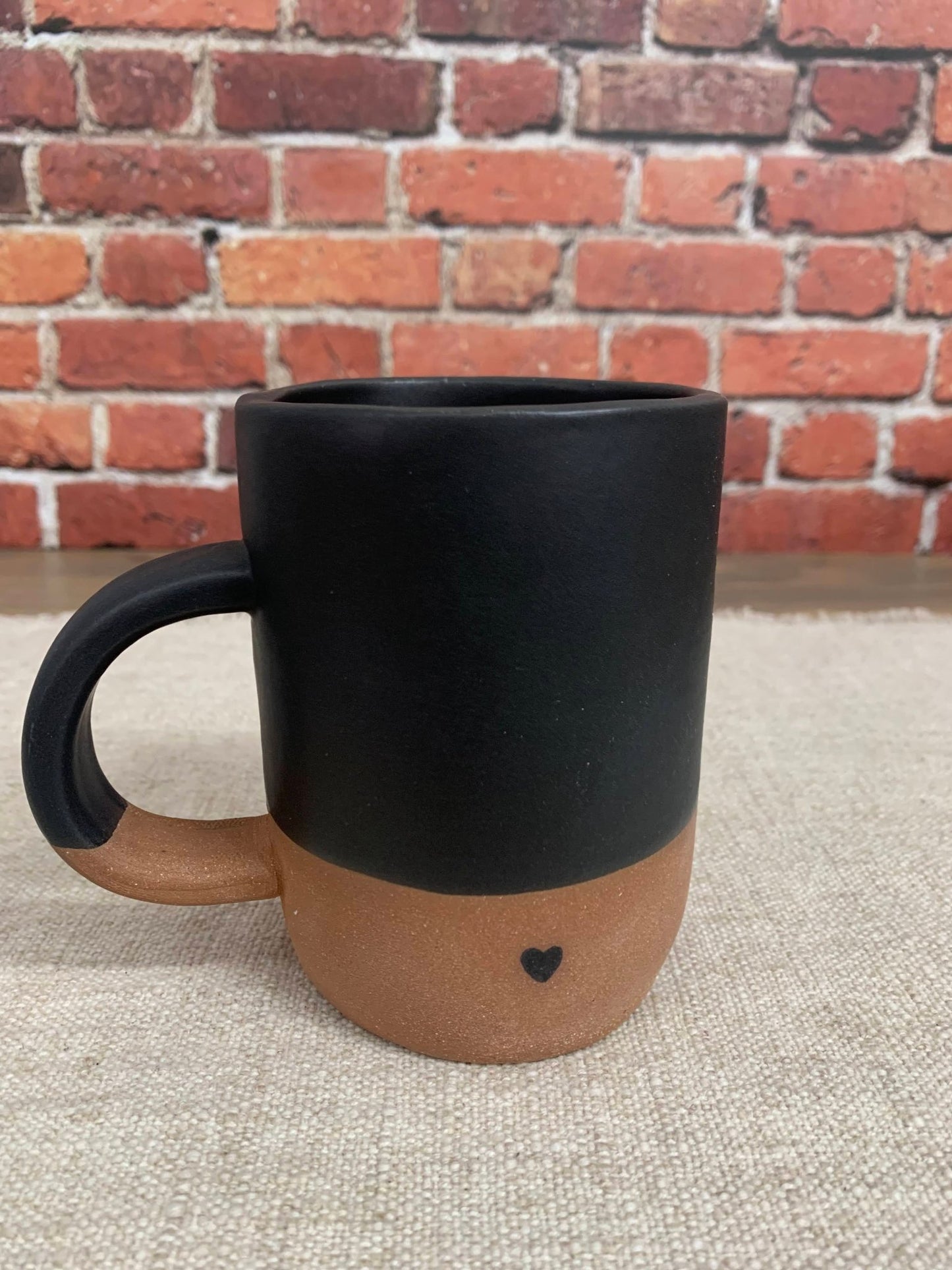 Black and brown ceramic mug with heart design on a textured surface and brick wall background