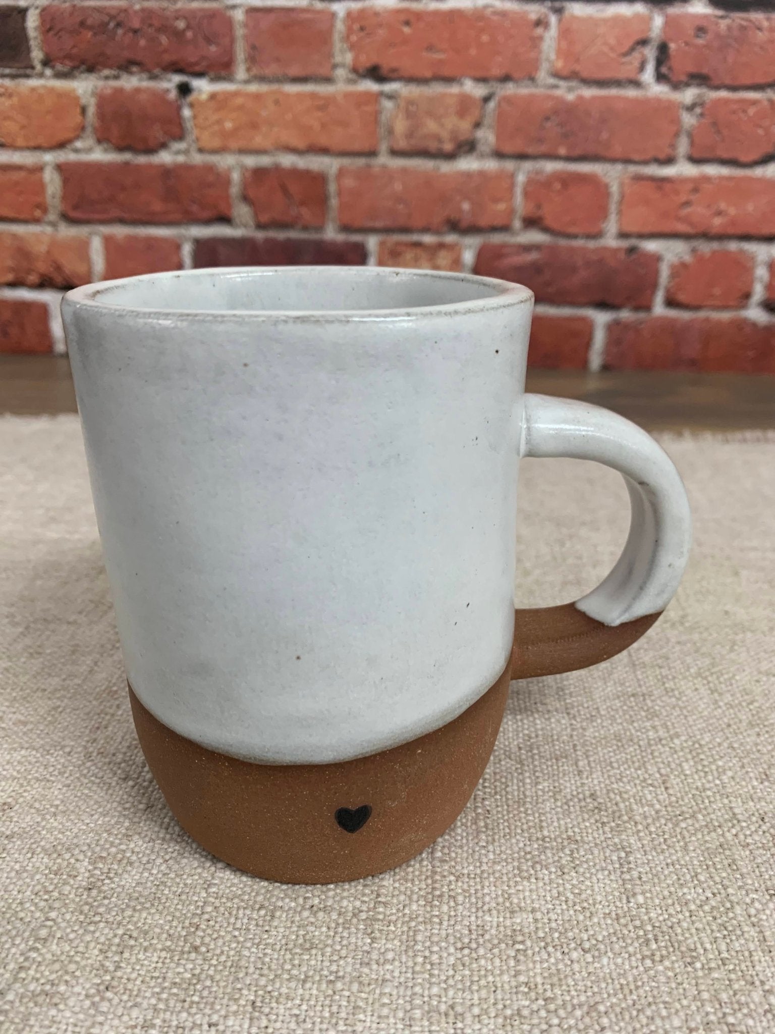 Ceramic pottery mug with a heart design against a brick wall.