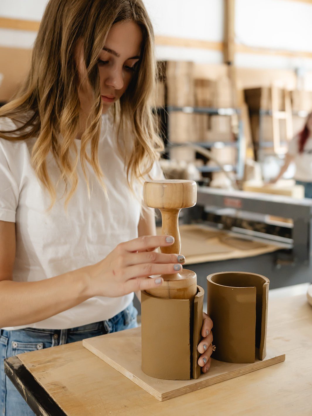 Woman holding a wood tool and ceramic mug in a ceramic art studio
