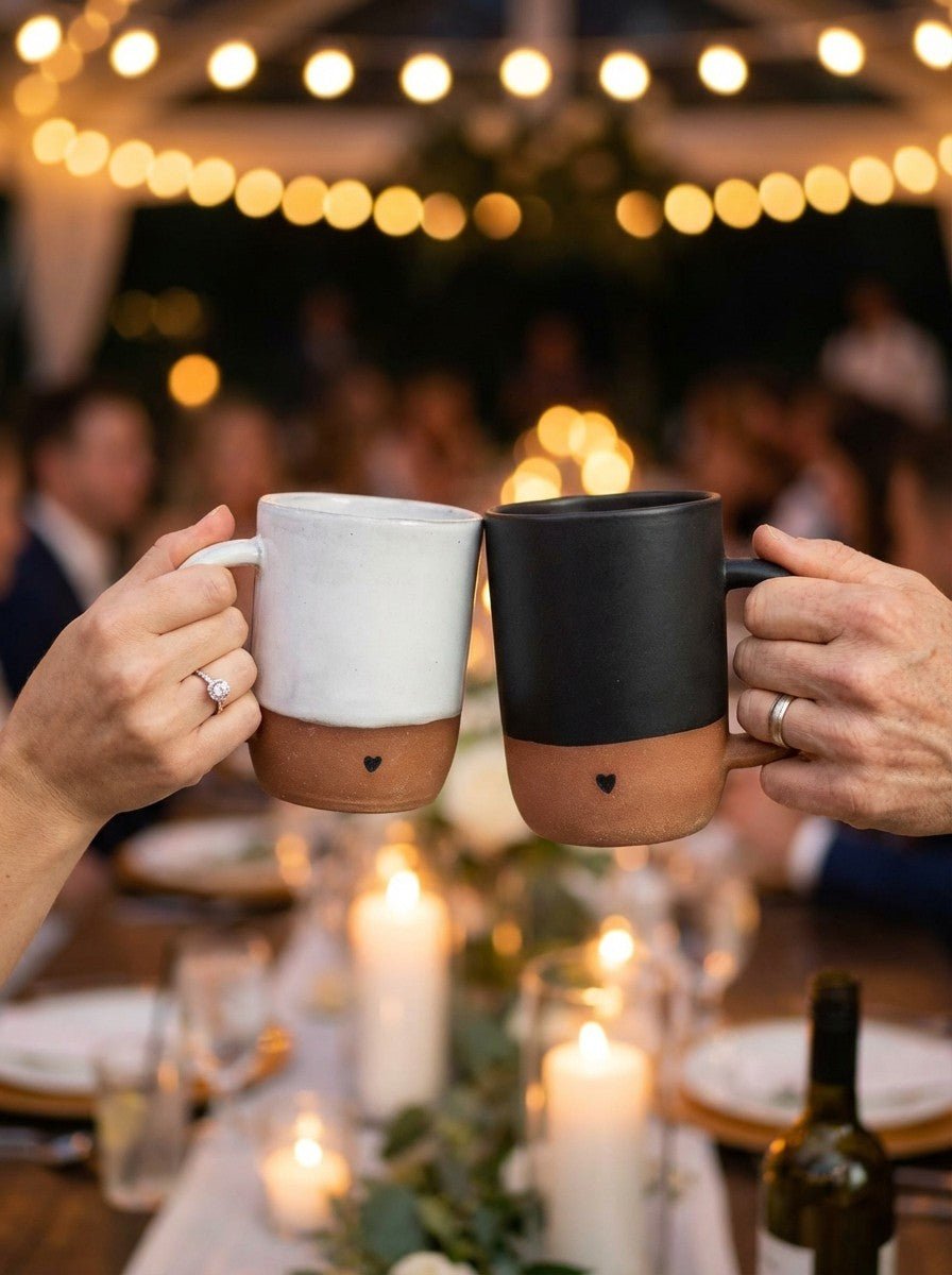 Two people holding a white and black mug together at a festive dinner table with string lights in the background.