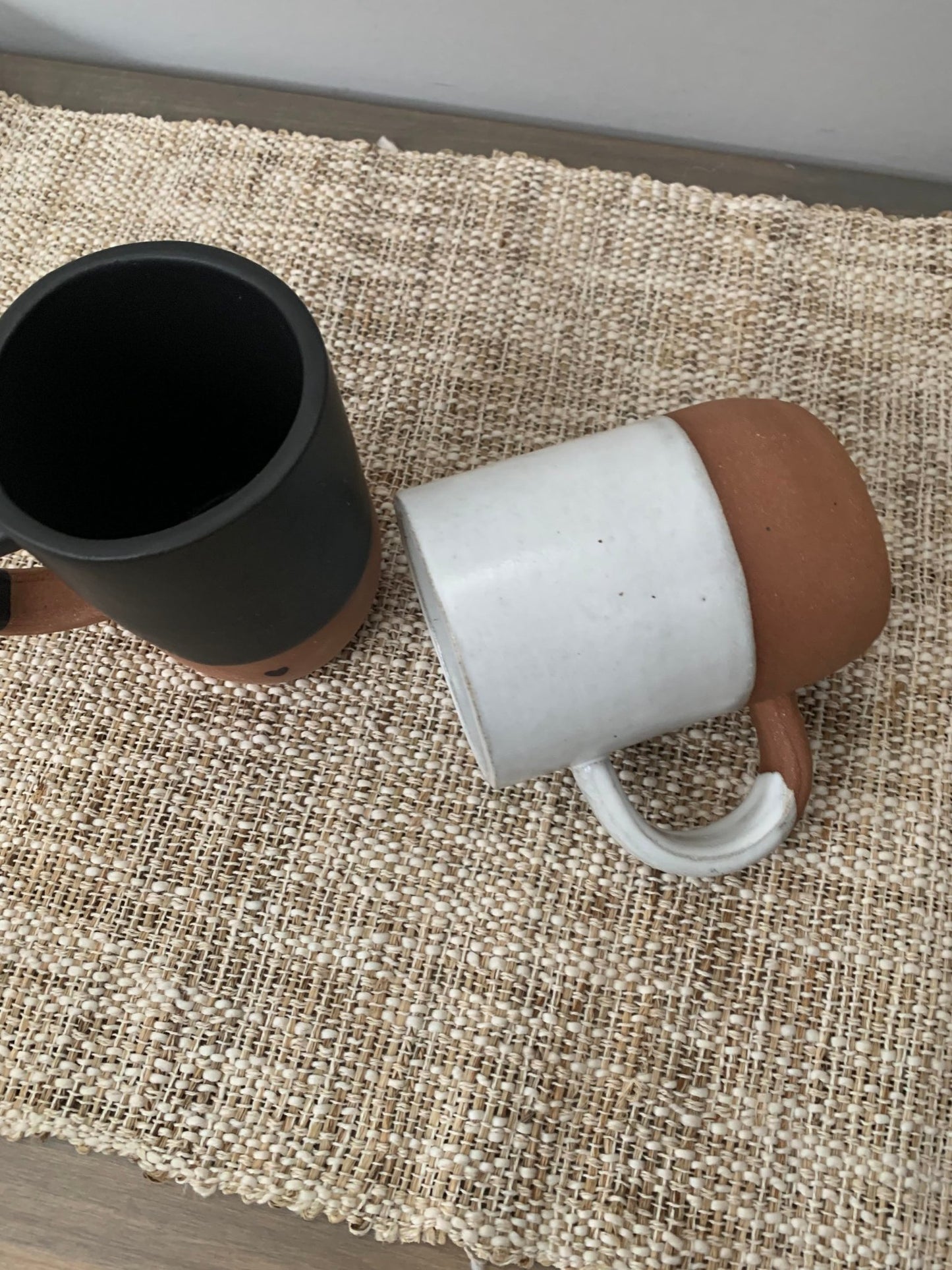 Two ceramic mugs, one white and one black, on a textured surface.