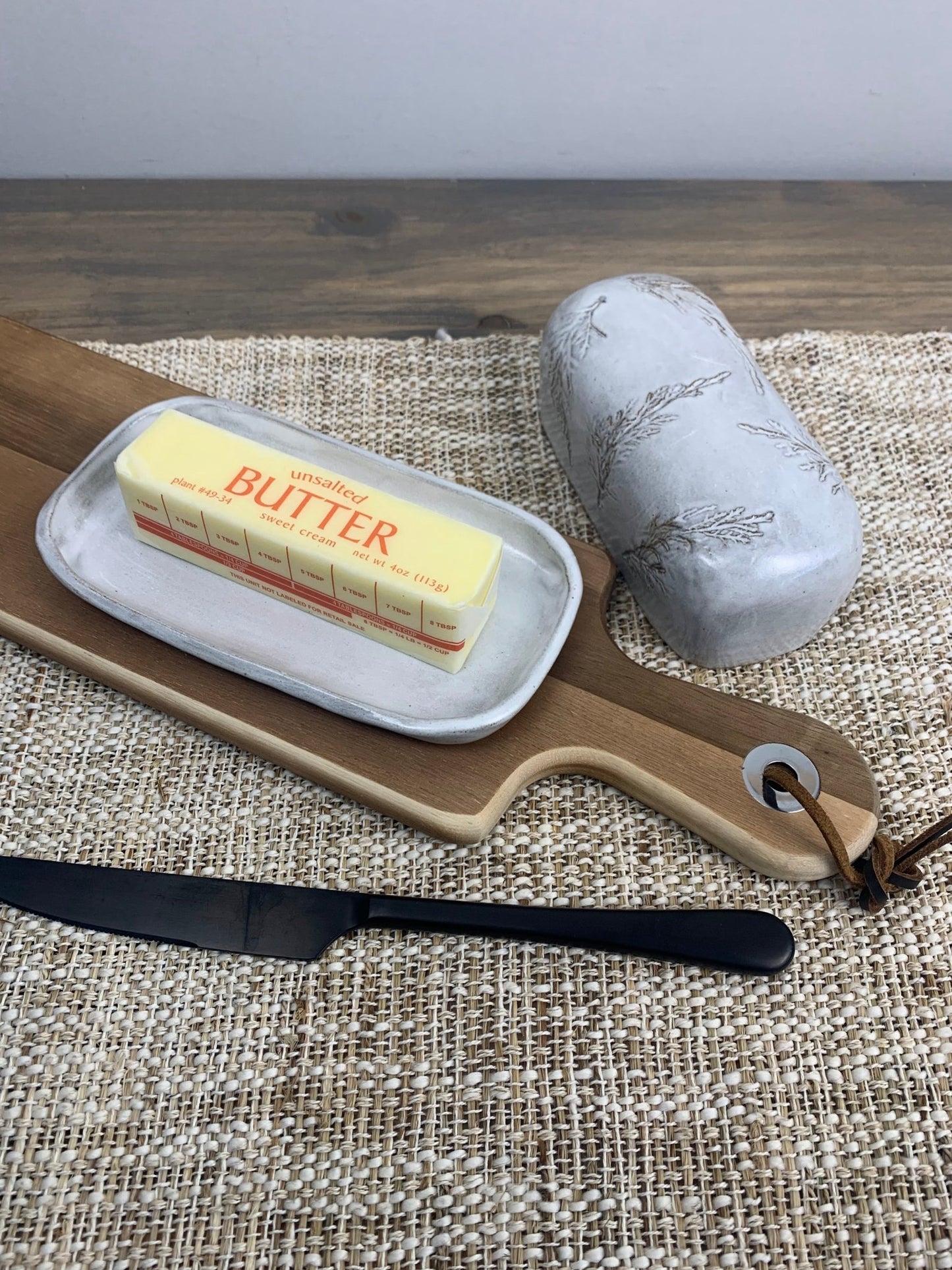 artisan botanical design Butter dish with a stick of butter and a knife on a woven mat.