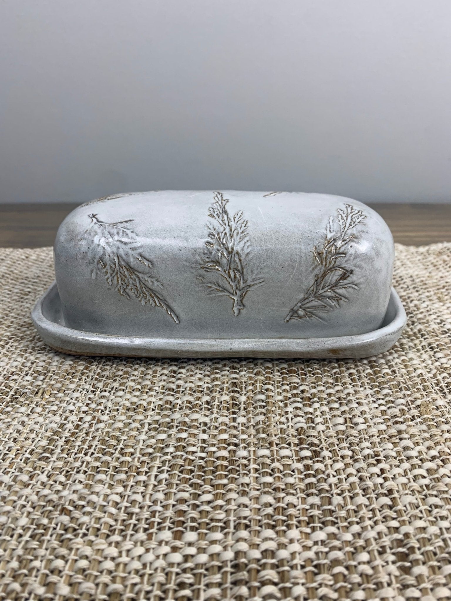 Decorative butter dish with fresh pine patterns on a textured surface