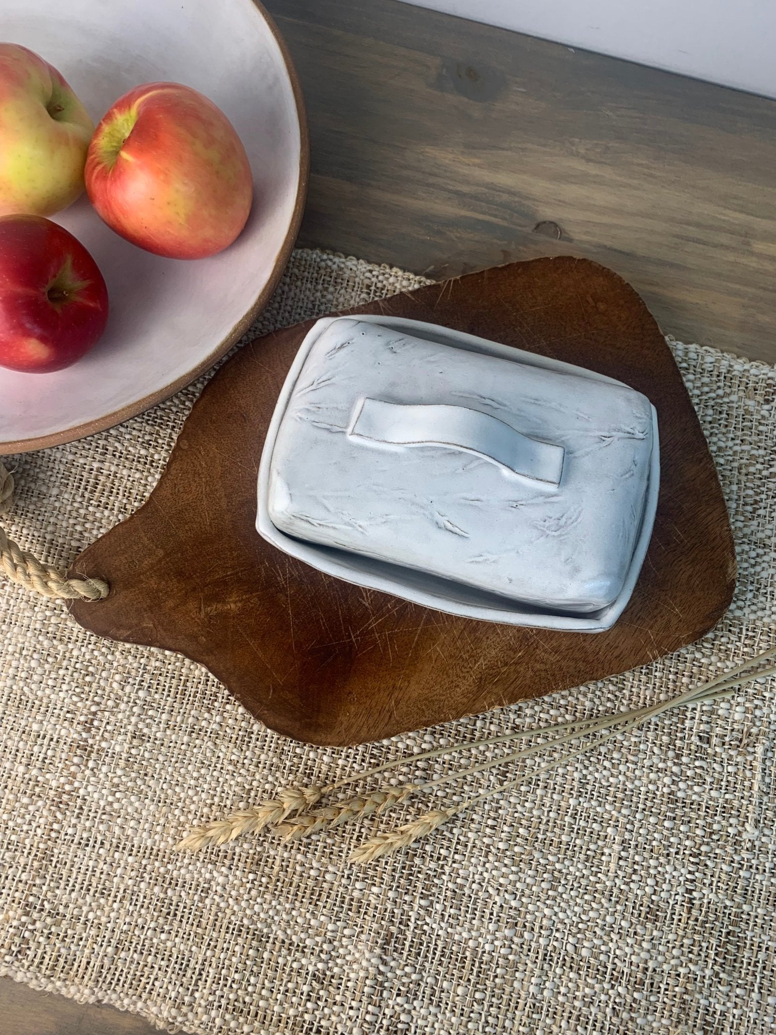 Handmade ceramic butter dish on a wooden cutting board with apples in the background