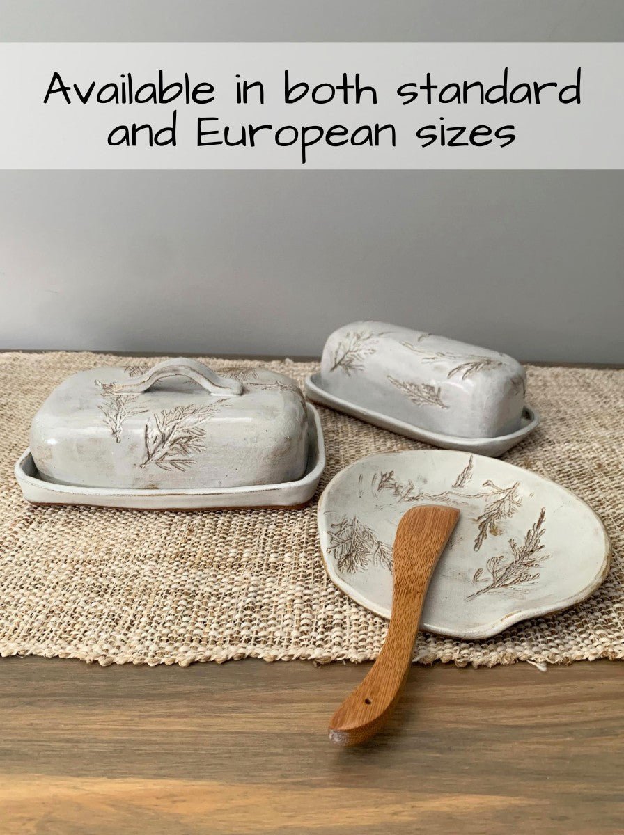 Set of handcrafted butter dishes with a wooden spoon on a textured surface.
