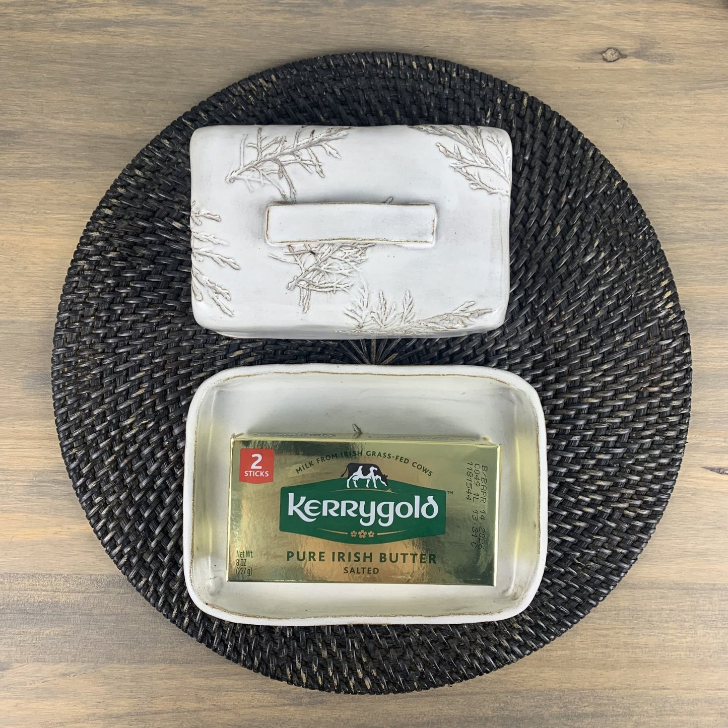 Handmade ceramic butter dish on a woven mat with a wooden surface background.