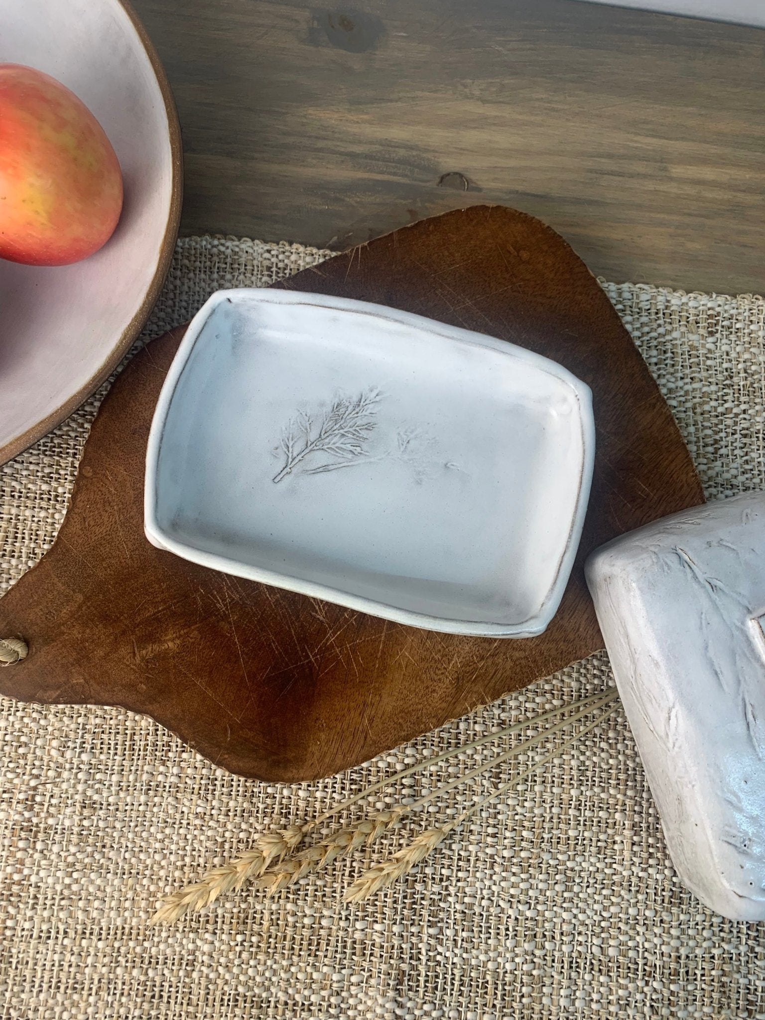 White handmade ceramic butter dish with leaf design on a wooden cutting board