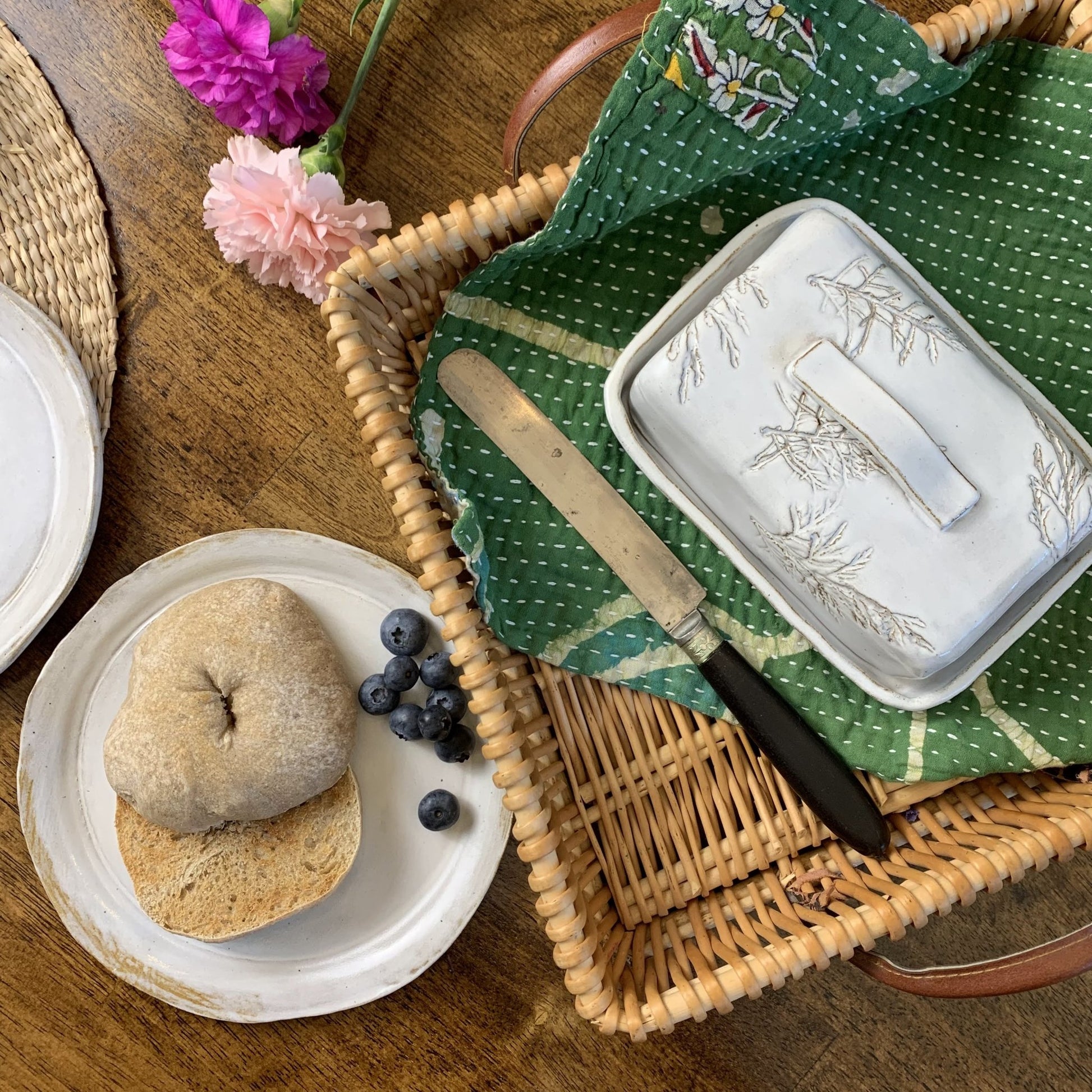 White handmade ceramic butter dish on wooden surface next to a bagel