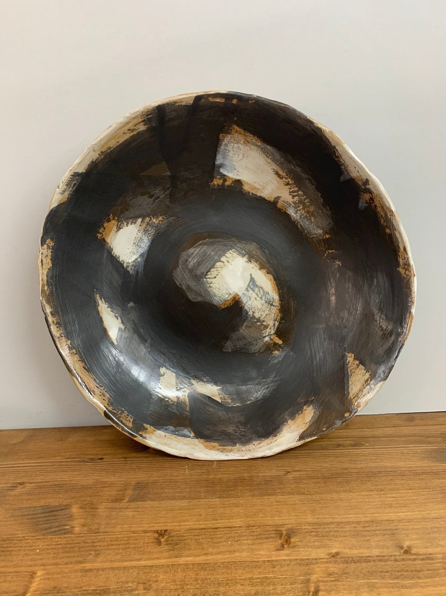 ceramic art  bowl with black, brown and white abstract circular design on a wood surface and light gray background