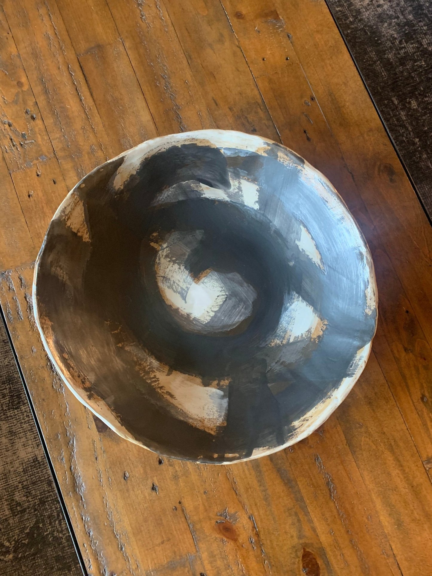 Ceramic art shallow bowl with black, brown and white circular design on a wood table