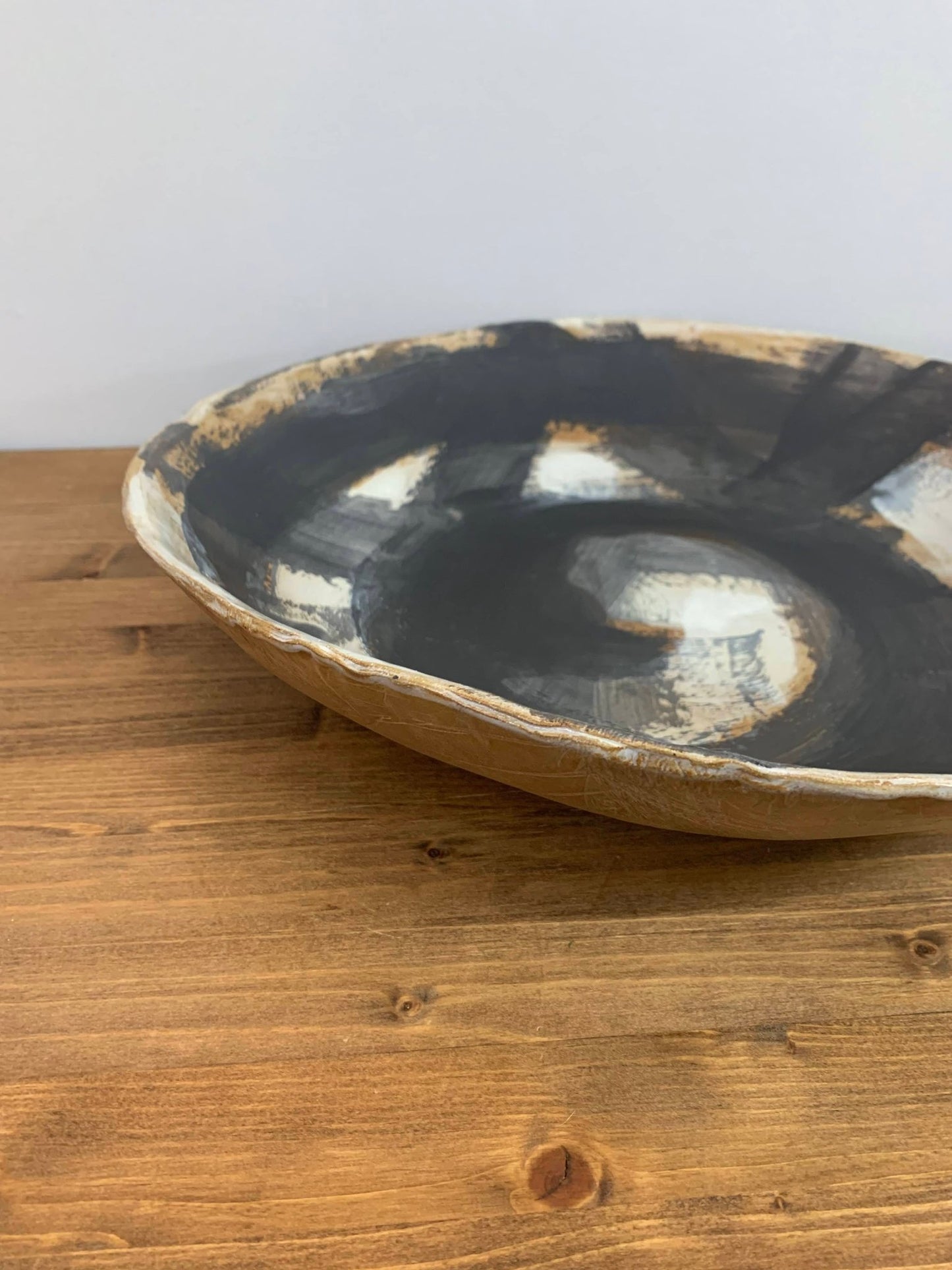 Ceramic art  bowl with black, brown and white abstract circular design on a wood surface and light gray background