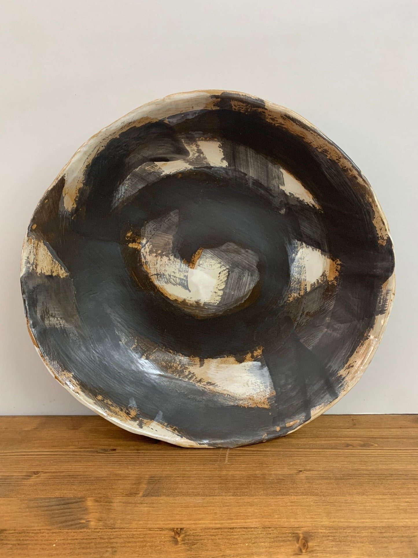 Ceramic art  bowl with black, brown and white abstract circular design on a wood surface and light gray background