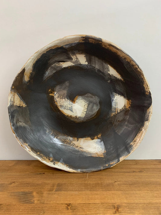 Ceramic art  bowl with black, brown and white abstract circular design on a wood surface and light gray background