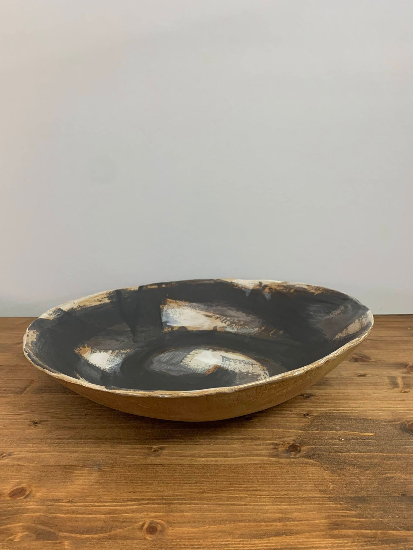 Ceramic art  bowl with black, brown and white abstract circular design on a wood surface and light gray background