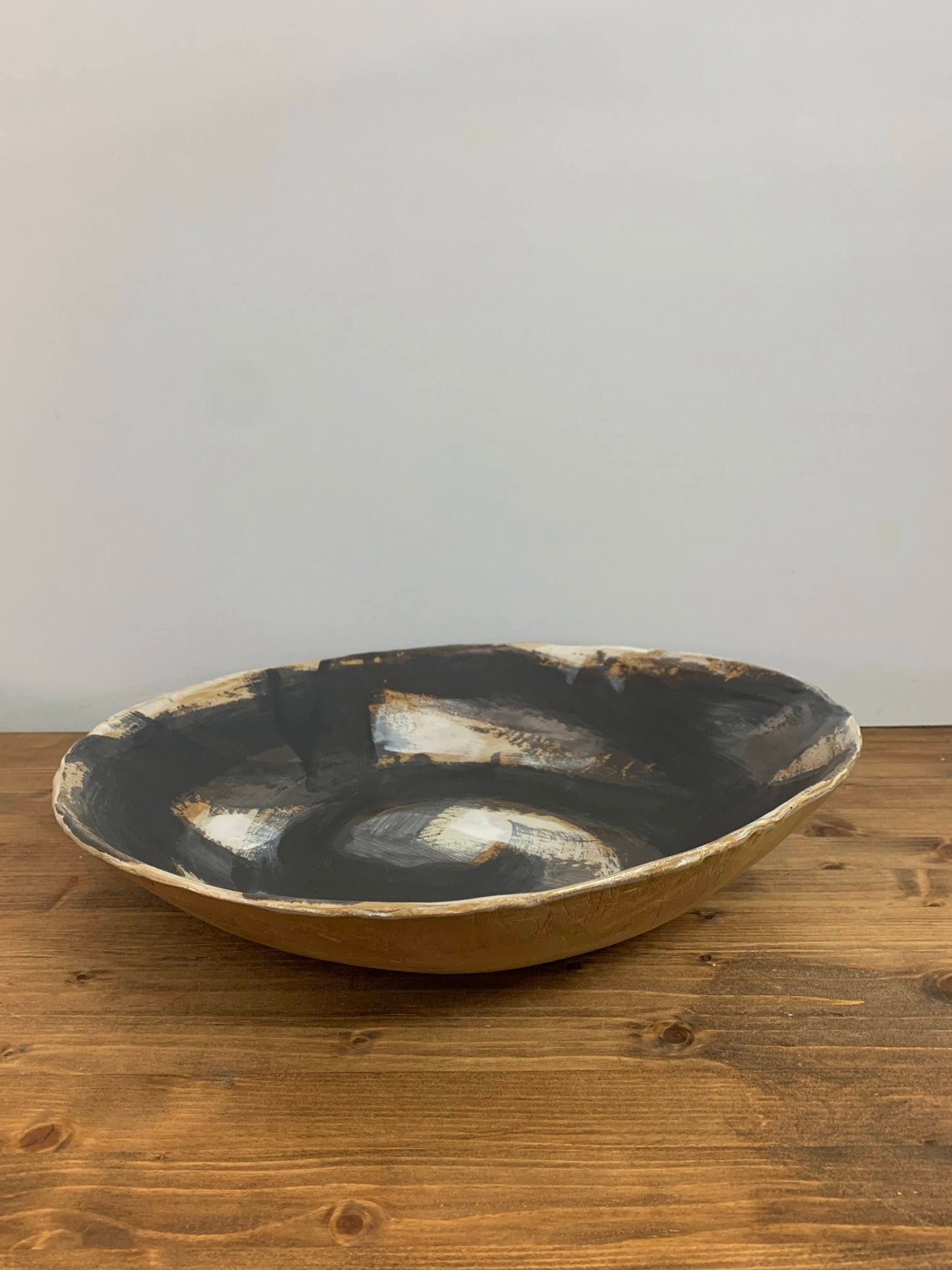Ceramic art  bowl with black, brown and white abstract circular design on a wood surface and light gray background