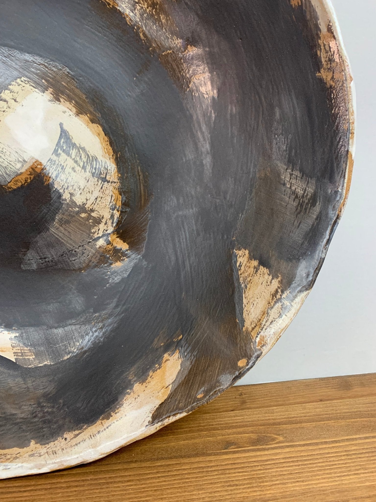 close-up of a Ceramic art shallow bowl with black, brown and white circular design on a wood surface and light gray background