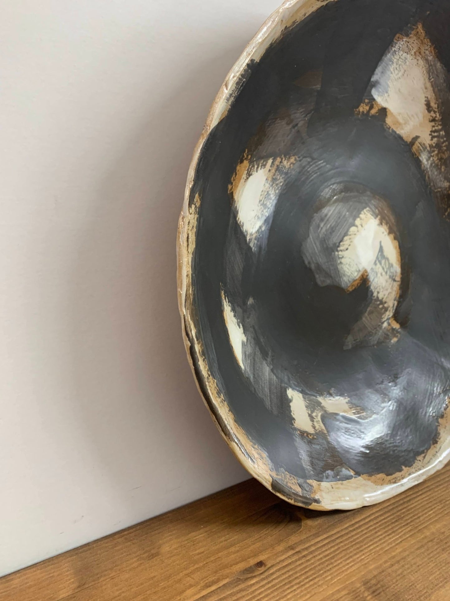 ceramic art  bowl with black, brown and white abstract circular design on a wood surface and light gray background