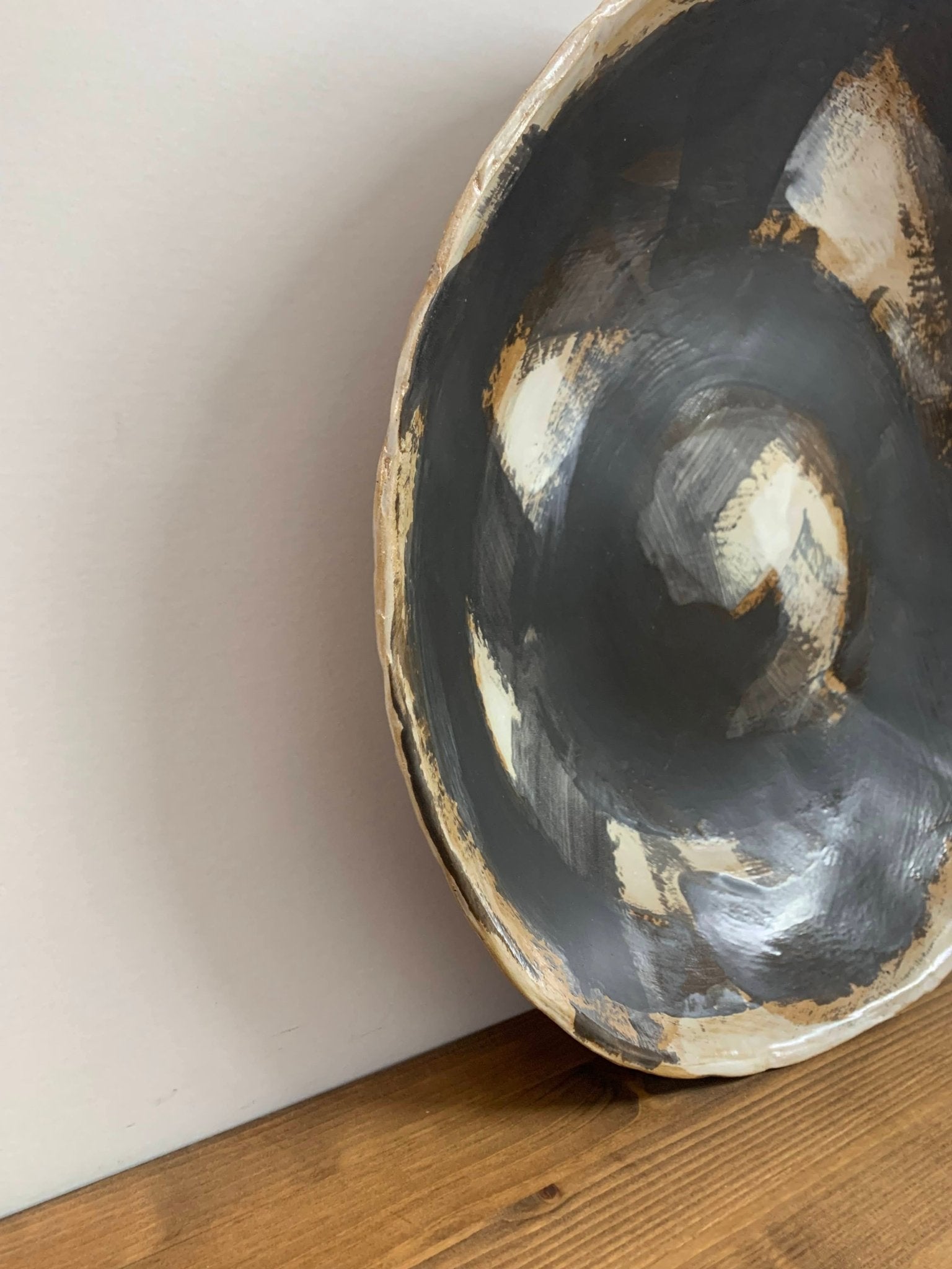 ceramic art  bowl with black, brown and white abstract circular design on a wood surface and light gray background