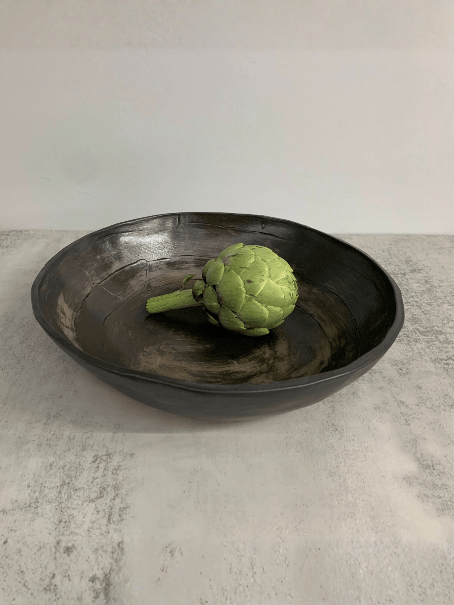 Green artichoke in a black stoneware  bowl on a light gray surface