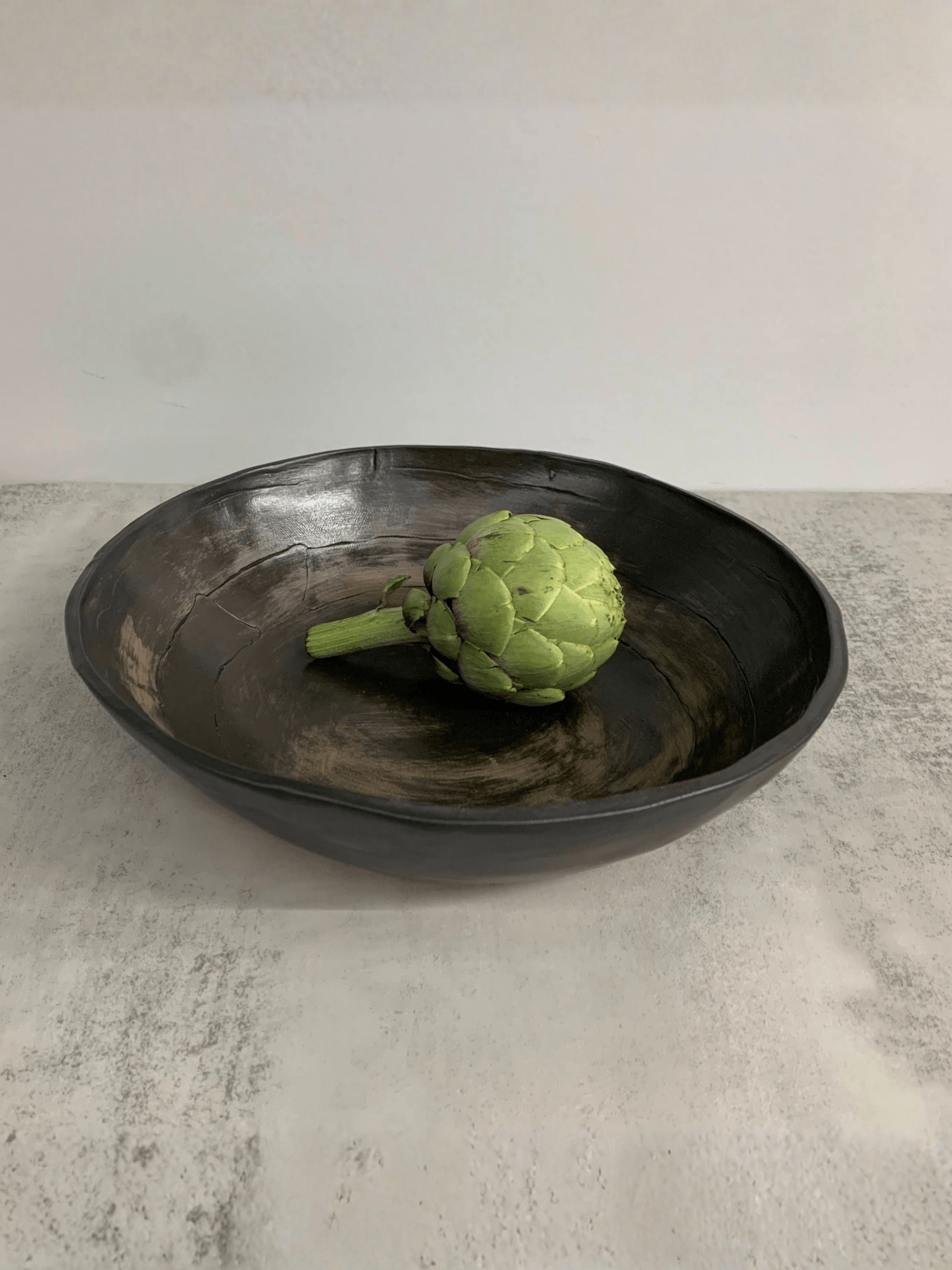 Green artichoke in a black stoneware  bowl on a light gray surface
