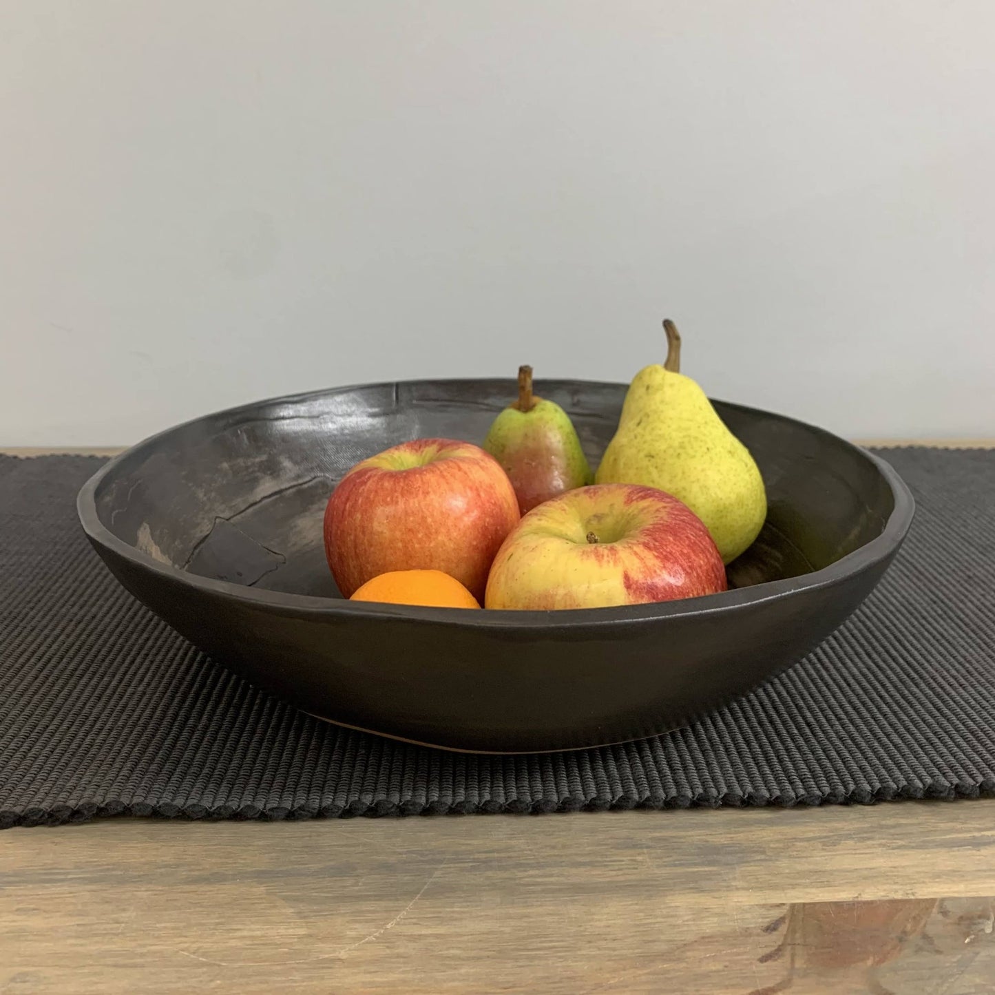 Black handmade ceramic bowl with apples and pears on a gray placemat